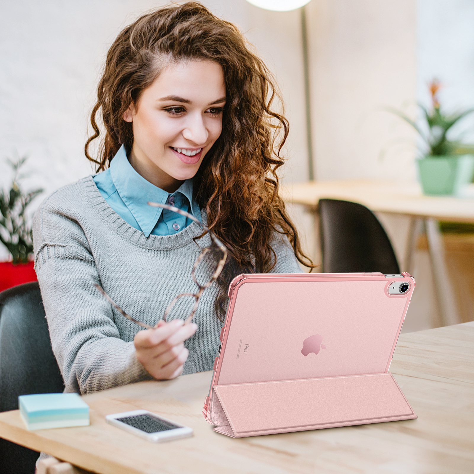 Eine Frau mit Brille hält eine weitere Brille und schaut auf ein rosa iPad.
