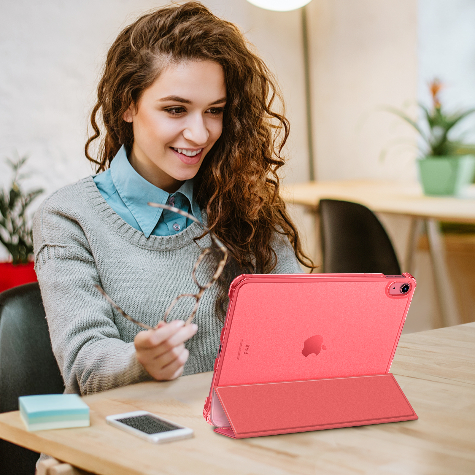 Frau hält Brille, lächelt auf rosa iPad in Hülle.