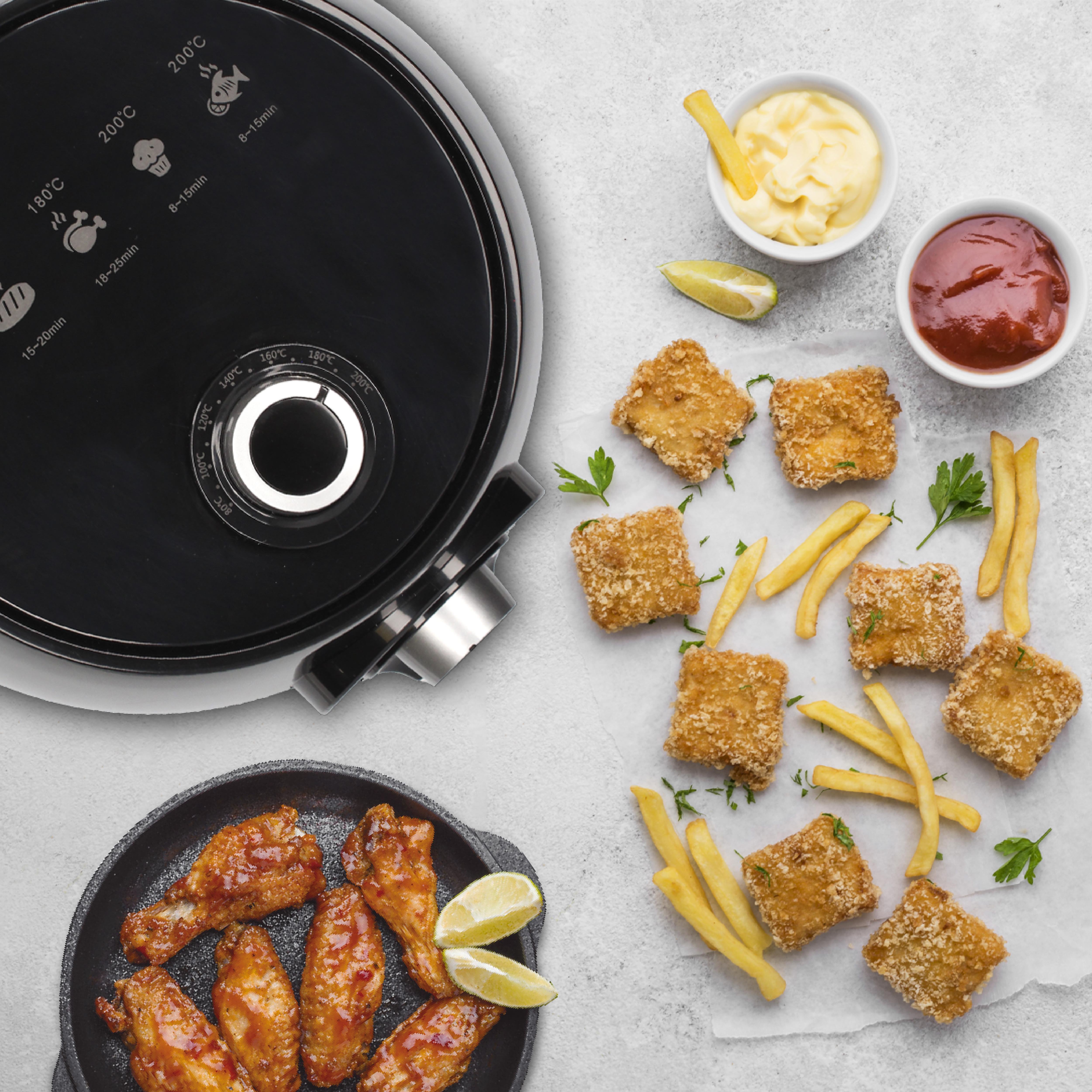 Vista superior de una freidora de aire, alitas, nuggets, papas fritas y salsas.