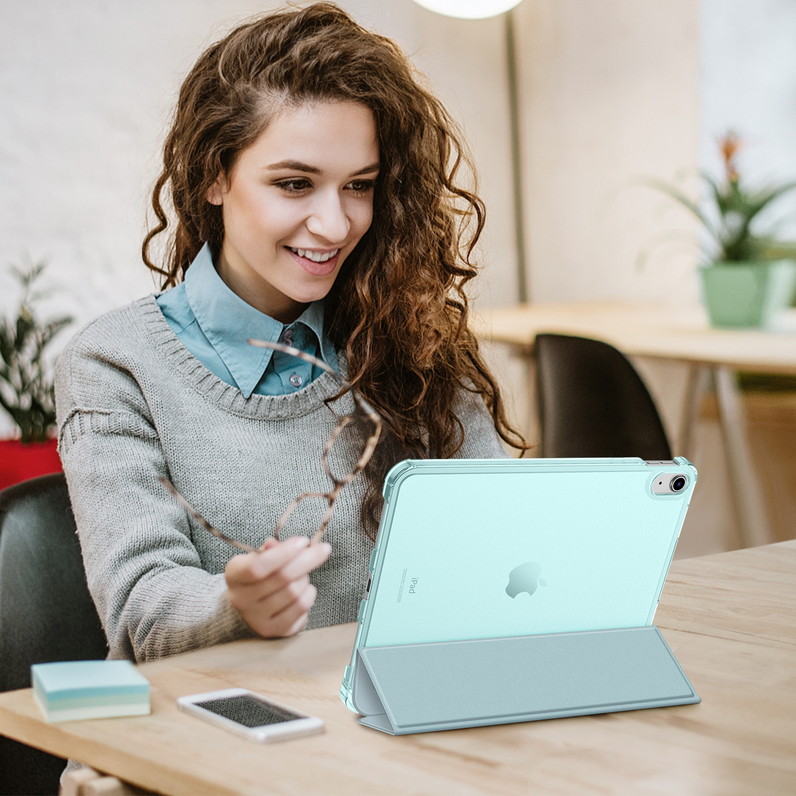 Frau hält Brille, benutzt Tablet. Text: iPad. Tablet ist mintgrün, Tisch ist Holz.