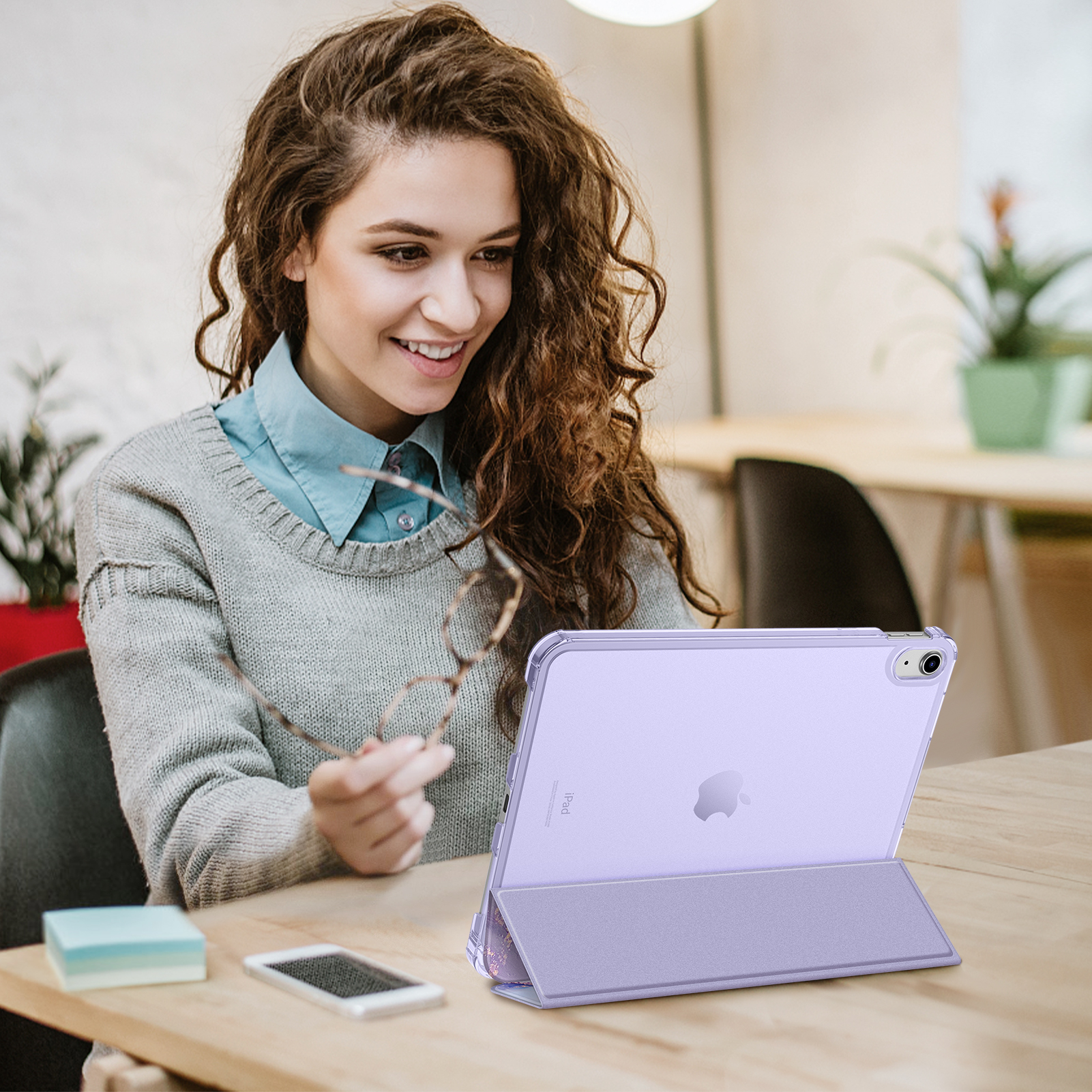 Frau mit Brille betrachtet ein lila iPad in einer Hülle an einem Tisch.