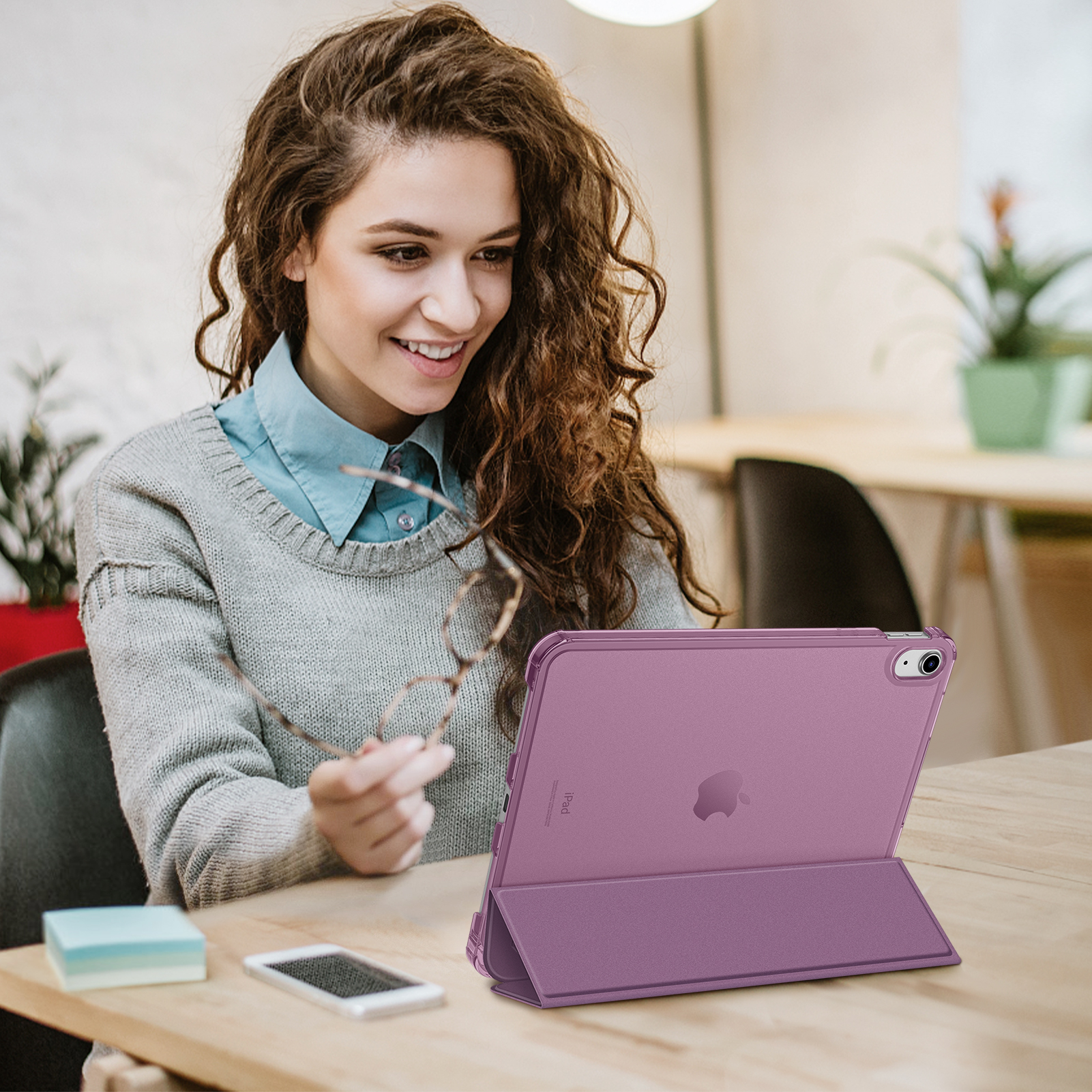 Frau mit Brille, blickt auf eine lila Tablet-Hülle auf einem Holztisch, neben einem Telefon.