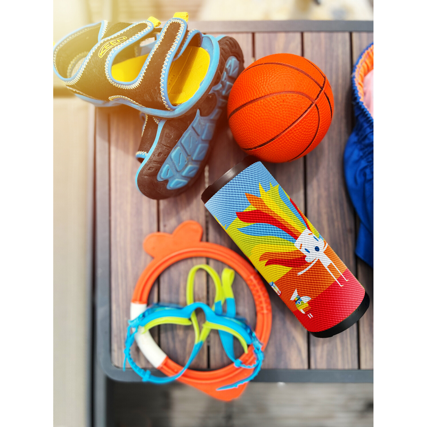 Draufsicht auf Basketball, Lautsprecher, Brille und Schuhe auf Holztisch. Sonnig.