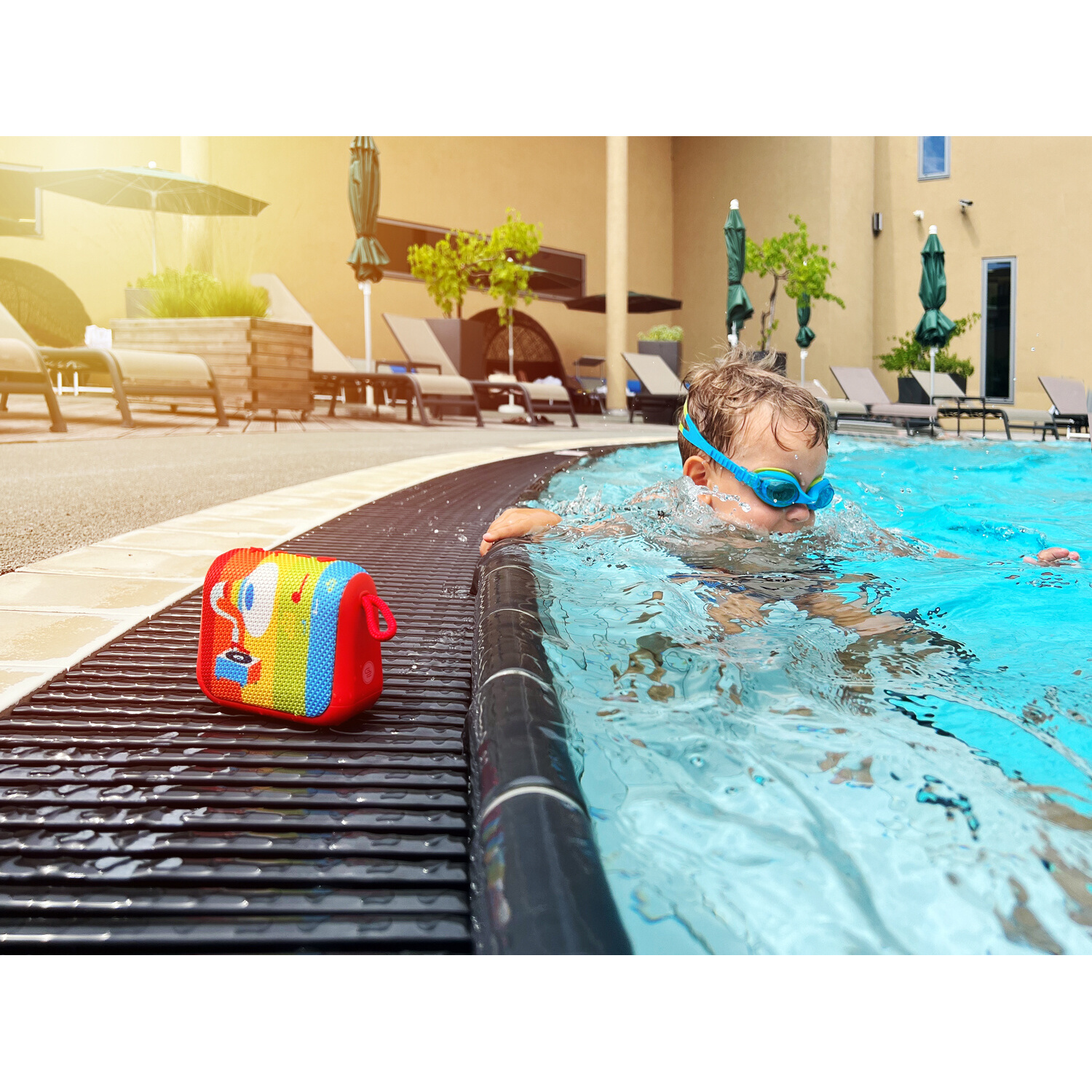 Junge mit Brille schwimmt im Pool neben einem bunten Lautsprecher.