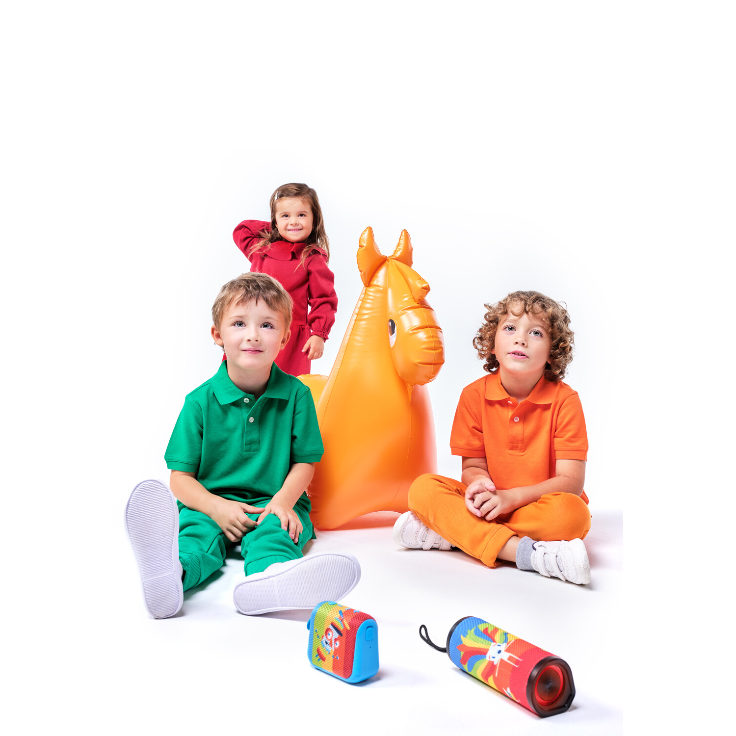 Kinder mit einem Spielzeugpferd und Lautsprechern. Ein Kind trägt Orange, andere Grün und Rot.