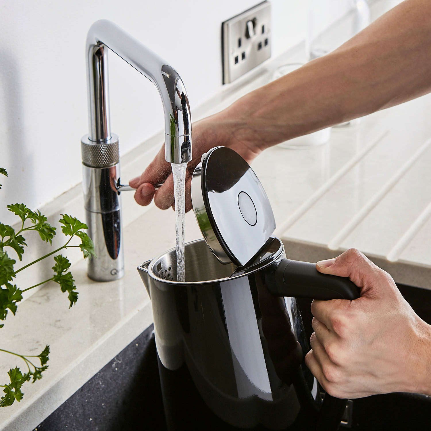 Eine Person füllt einen schwarzen Wasserkocher mit Wasser aus einer Chromarmatur.