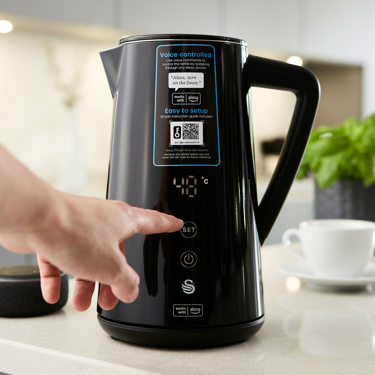 Schwarzer Wasserkocher mit Hand, die auf dem Bildschirm „SET“ drückt. Text und Alexa-Logo.