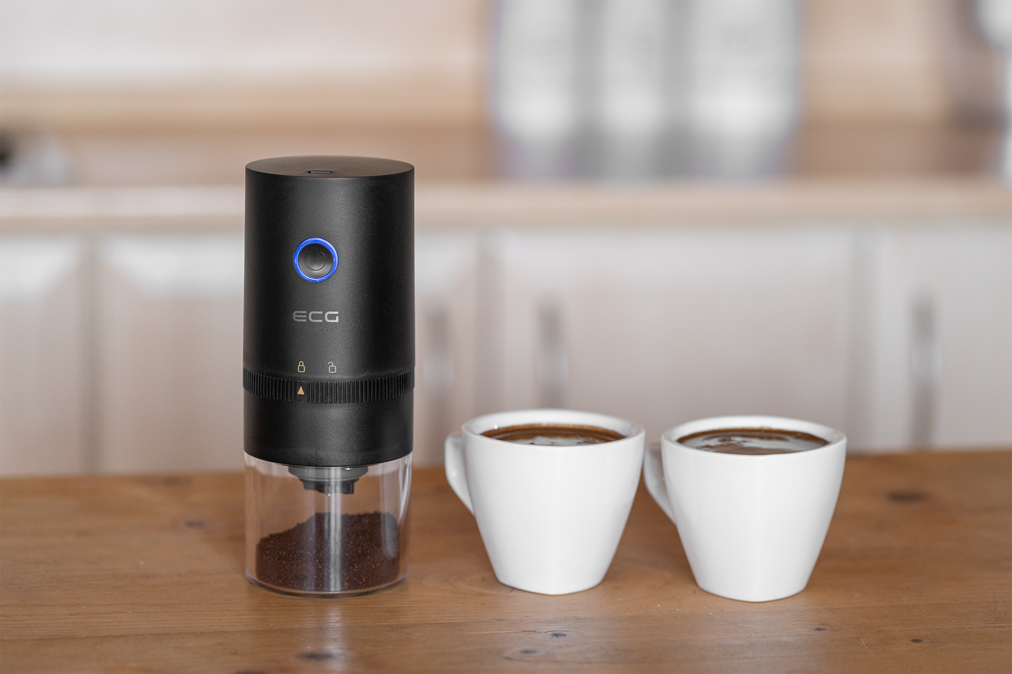 Czarny młynek do kawy z kawą i dwoma białymi filiżankami na drewnianej powierzchni.