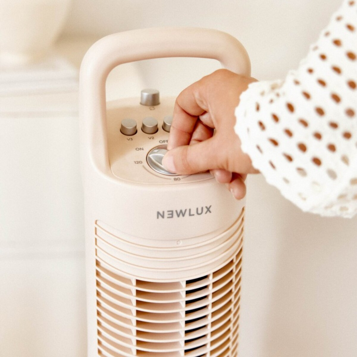 Una mano ajustando la configuración en un purificador de aire beige vertical. Tiene botones y un dial.