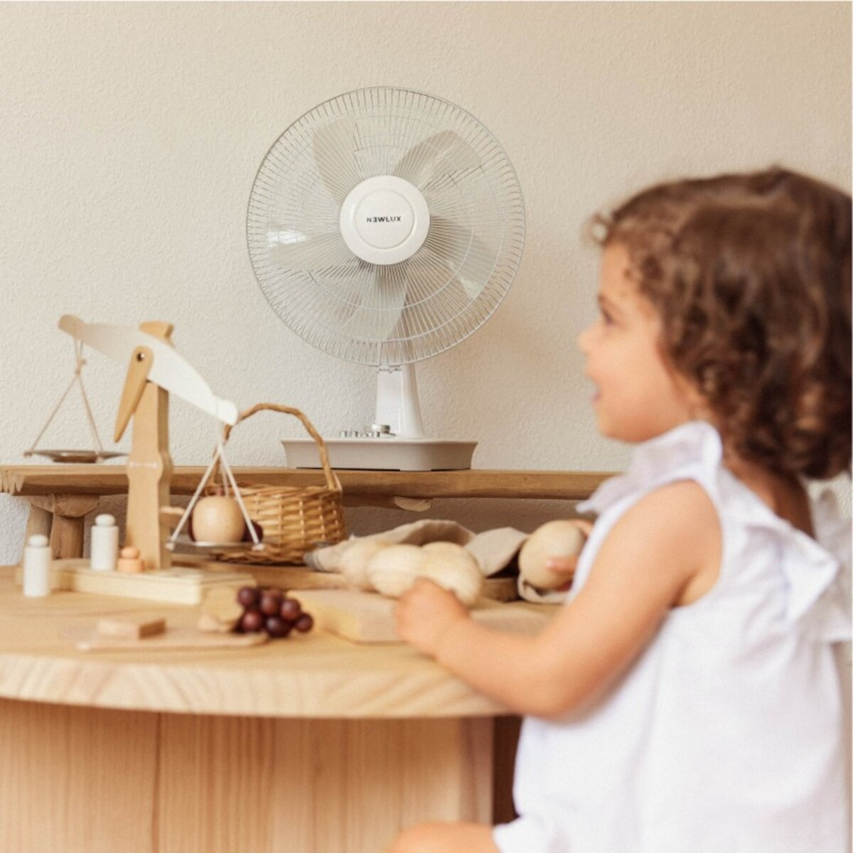 Un niño mirando una mesa con balanzas, juguetes y un ventilador al fondo.
