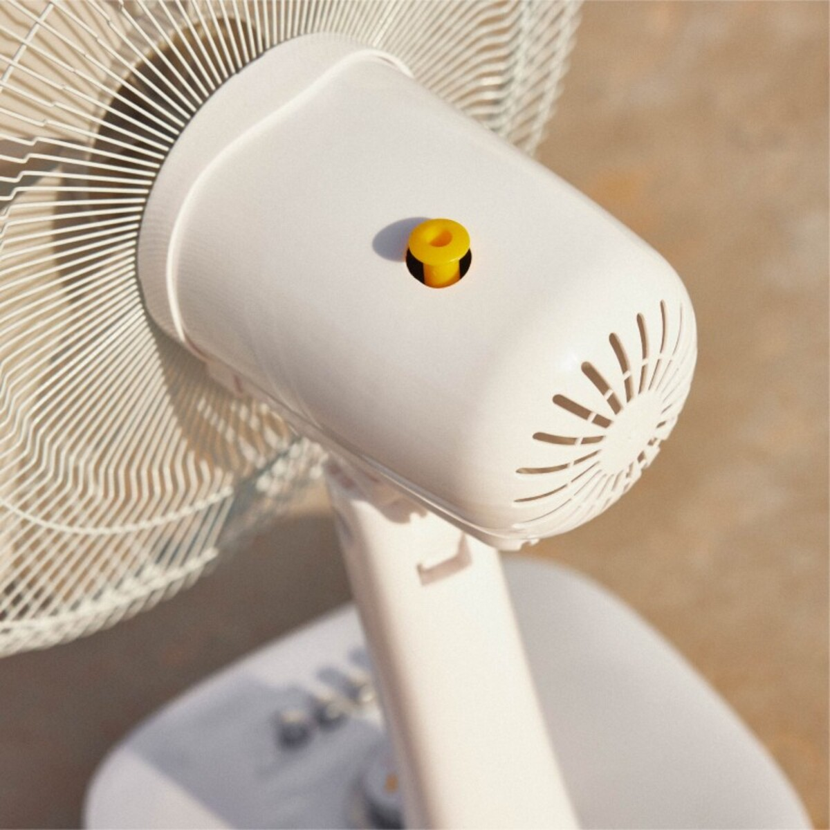 Primer plano de un ventilador blanco con un botón amarillo en la parte superior. Las aspas son visibles.