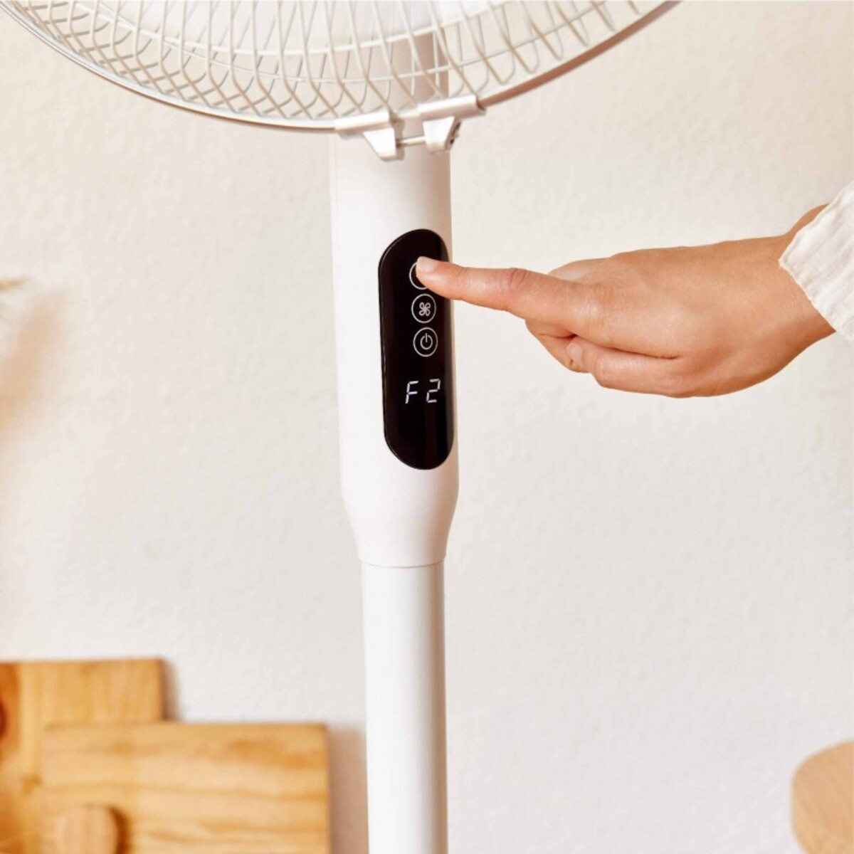 Una mano presiona un botón en un ventilador blanco. El ventilador está en un soporte blanco.