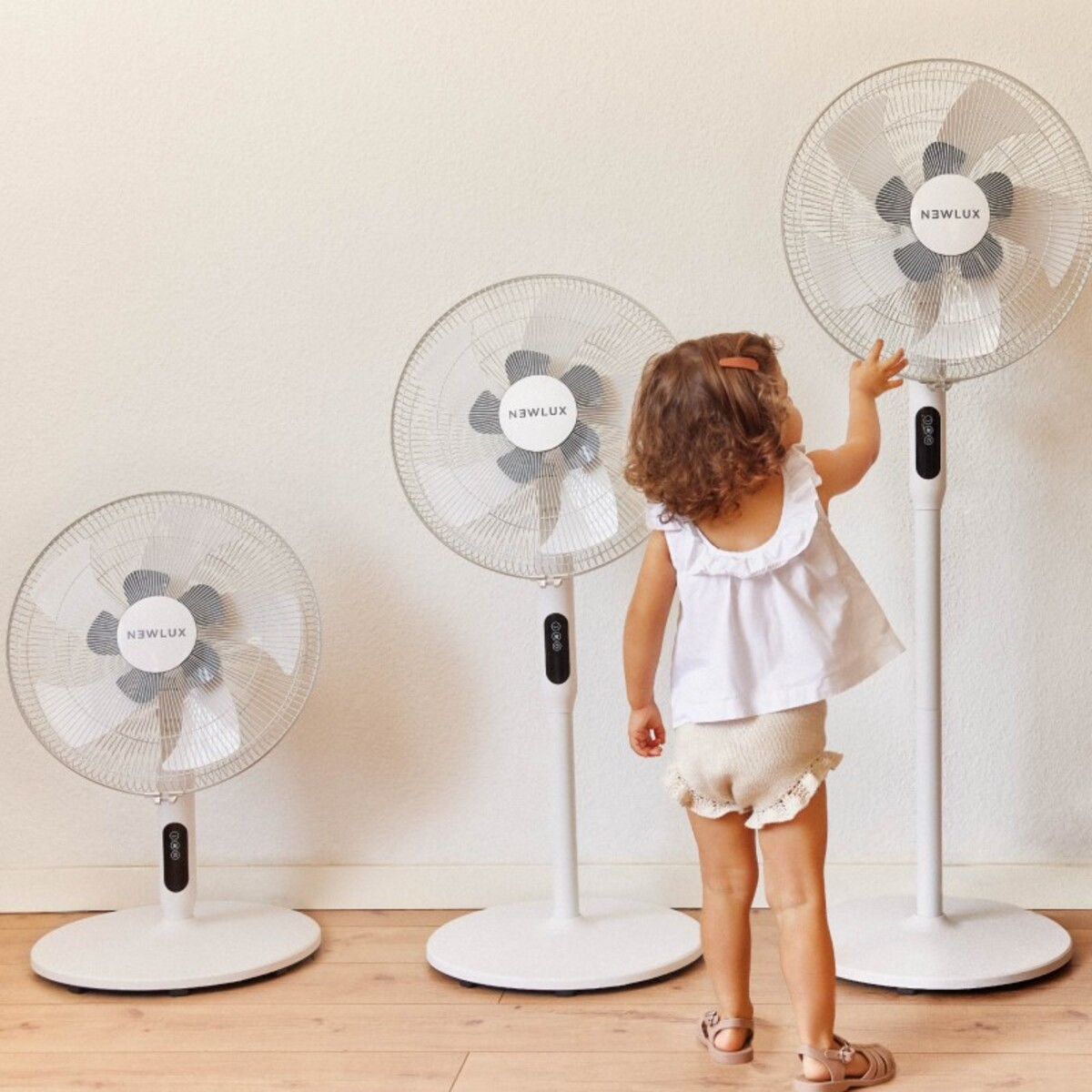 Un niño alcanza a un ventilador de pie. Otros dos ventiladores en el fondo.