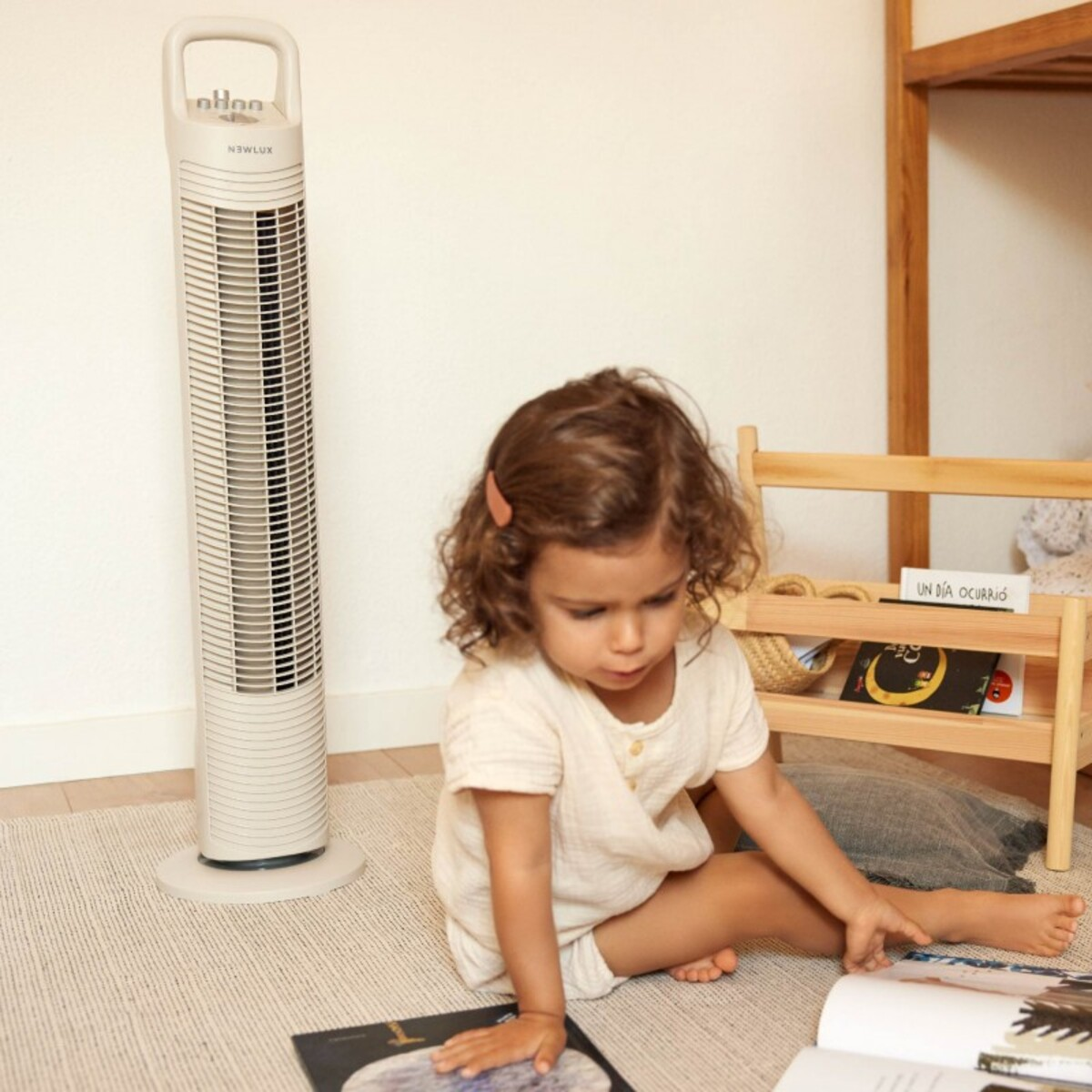 Niña leyendo en el suelo, con ventilador y estantería en el fondo.