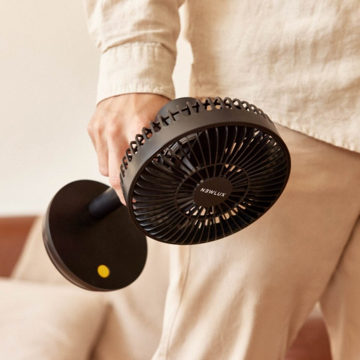 Persona sosteniendo un ventilador portátil negro. El ventilador es negro y tiene un botón amarillo.