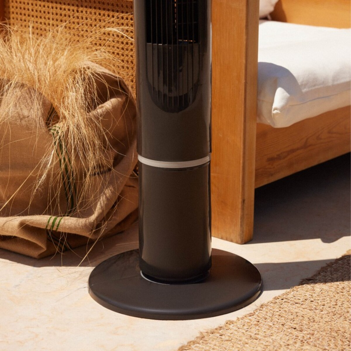 Ventilador de torre negro sobre una superficie de piedra. Una bolsa marrón detrás, con hierba seca.