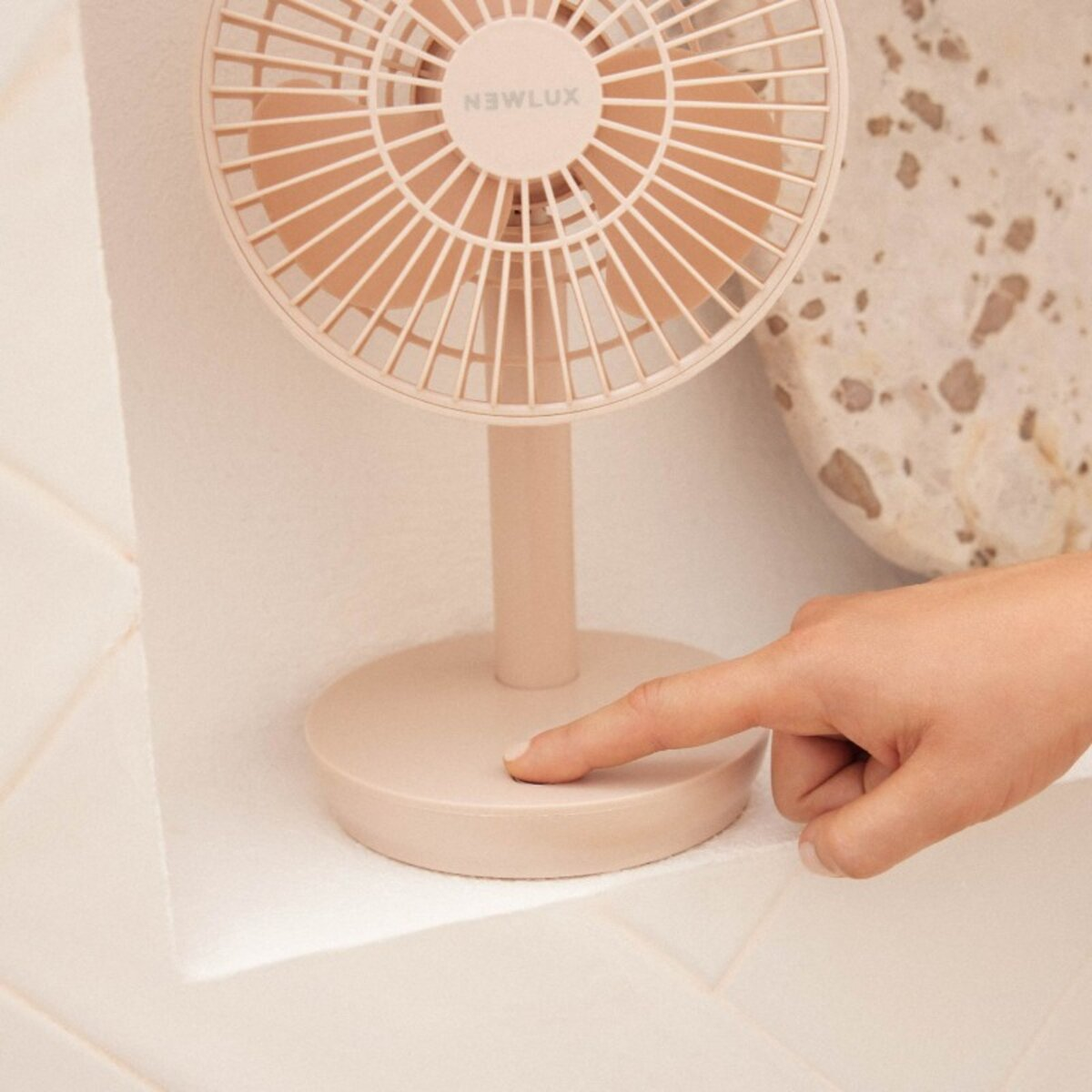 Un pequeño ventilador rosa con un dedo presionando el botón de la base.