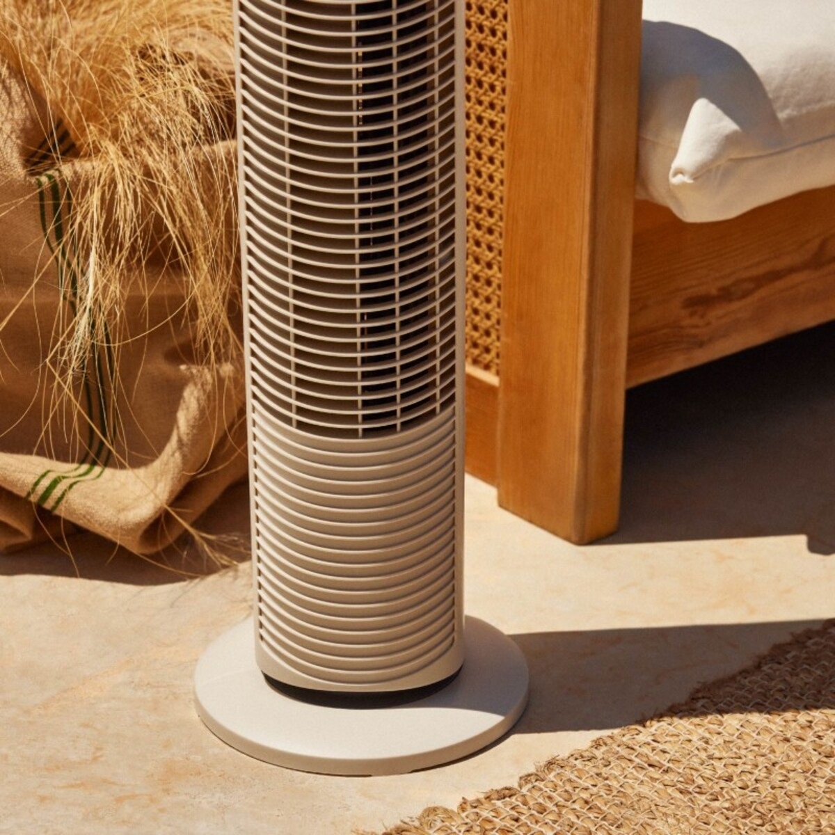 Un ventilador de torre beige en un patio con una alfombra tejida y hierba seca.