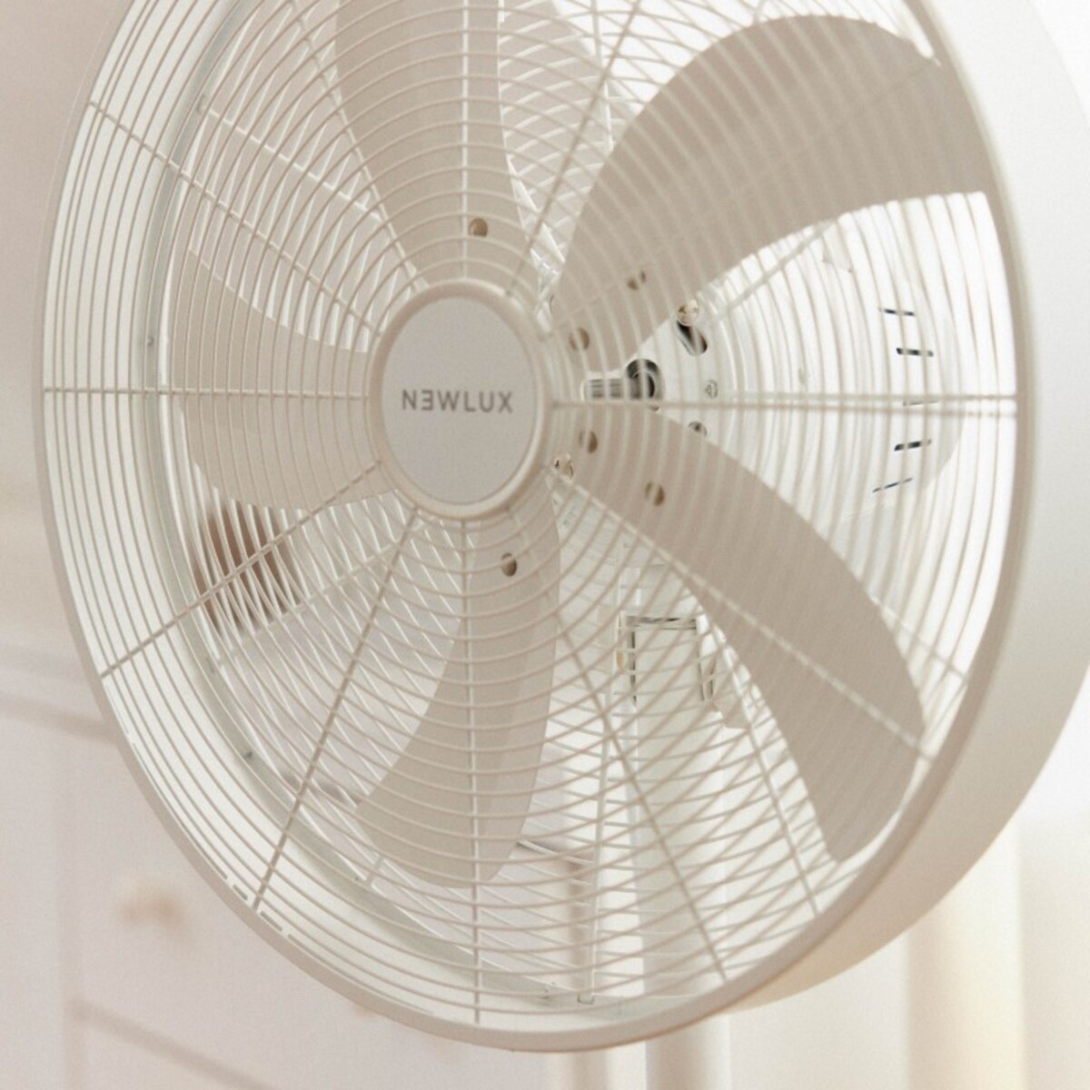 Un ventilador blanco con aspas curvas, vista de cerca. La marca es 'NEWLUX'.