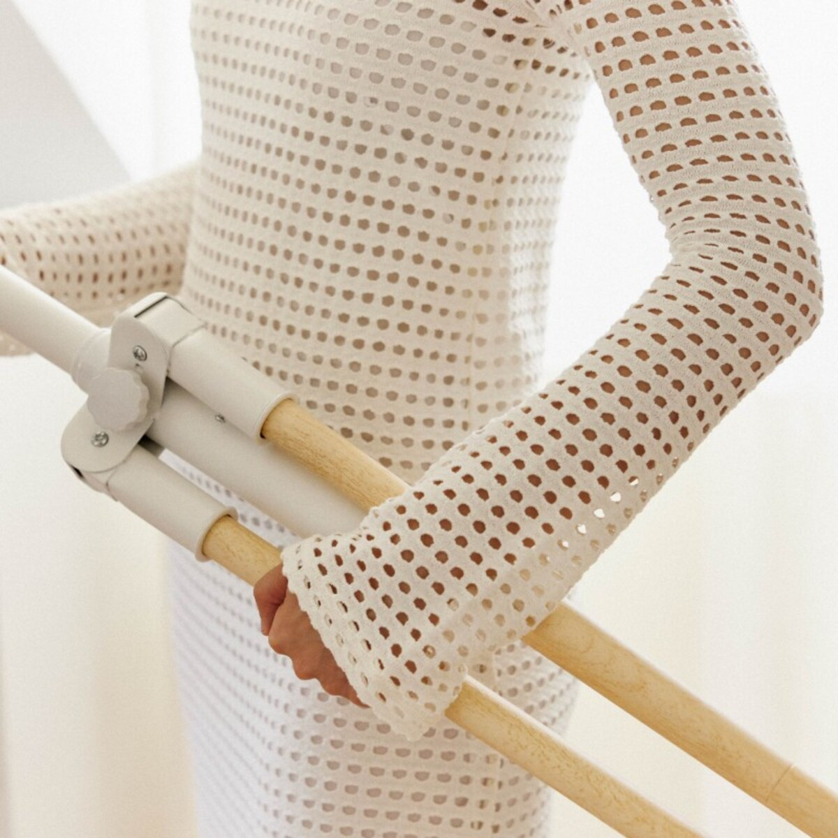 Persona sosteniendo una estructura blanca con varillas de madera, vistiendo un vestido blanco calado.