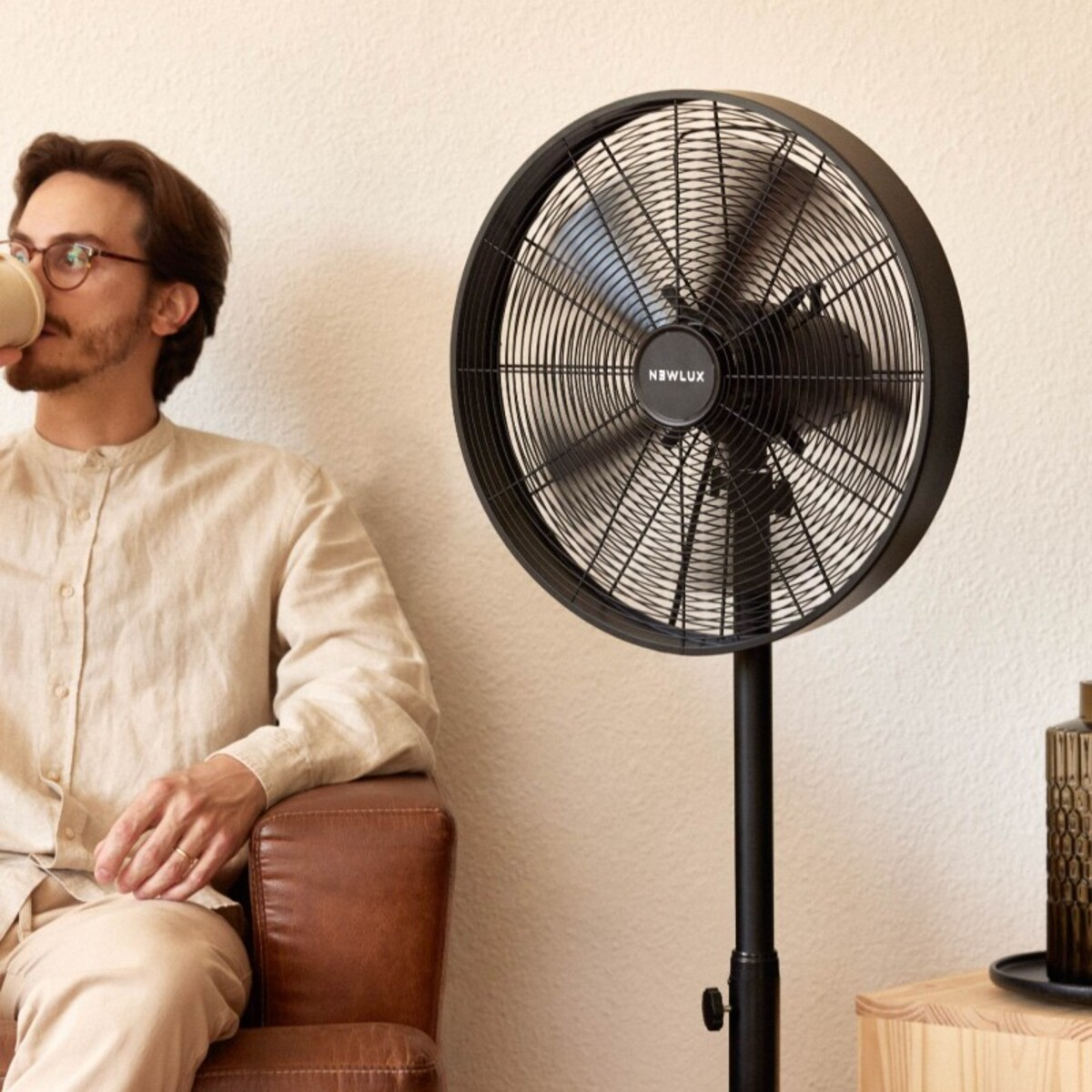 Hombre sentado cerca de un ventilador de pie negro.