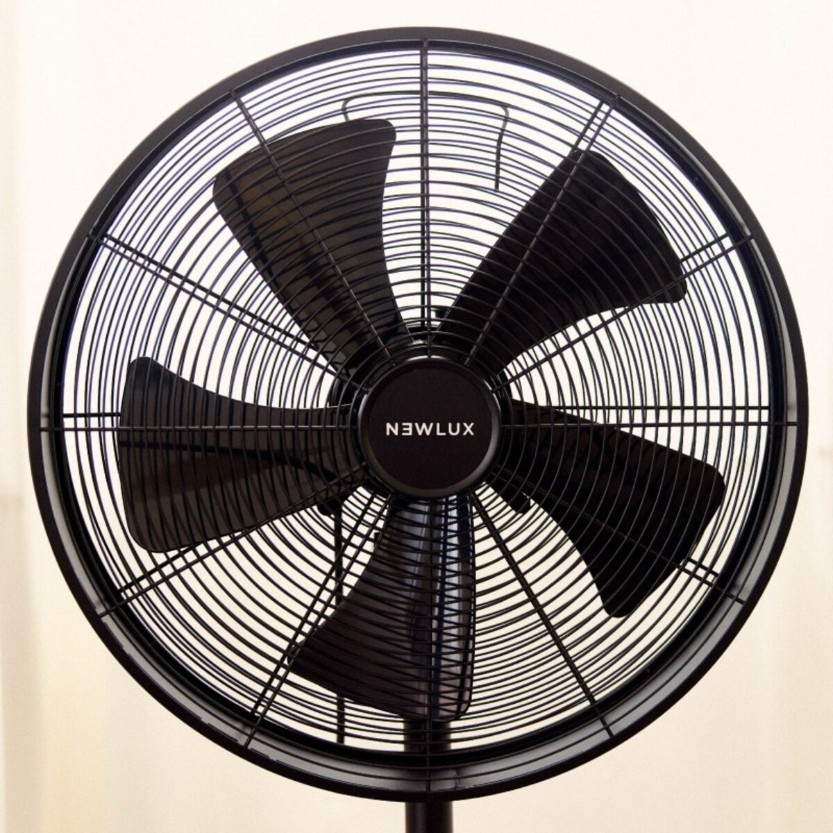 Ventilador de pie negro. Tiene cuatro aspas negras y una jaula protectora redonda. El ventilador está sobre un soporte negro.
