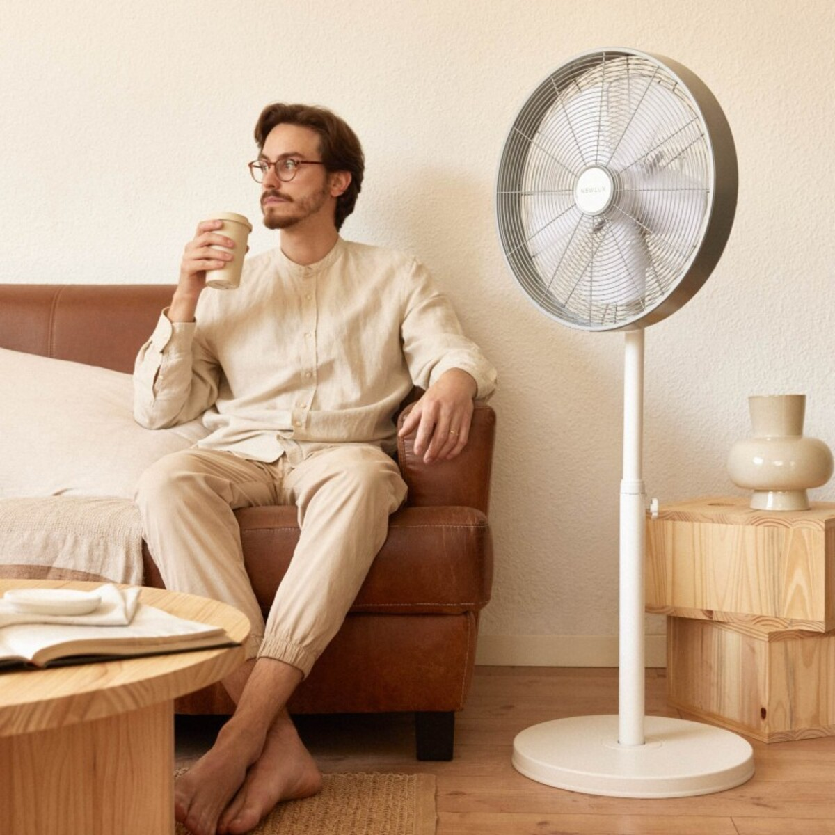 Hombre sentado con una taza de café, un ventilador detrás. Usa gafas y ropa casual.