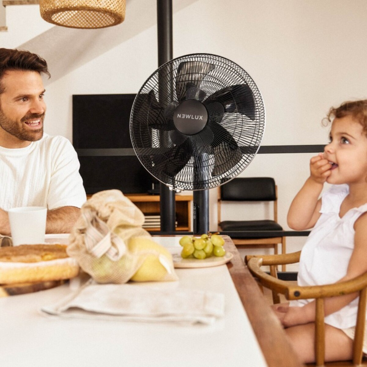 Un hombre y una niña en una mesa con un ventilador negro y algo de comida.