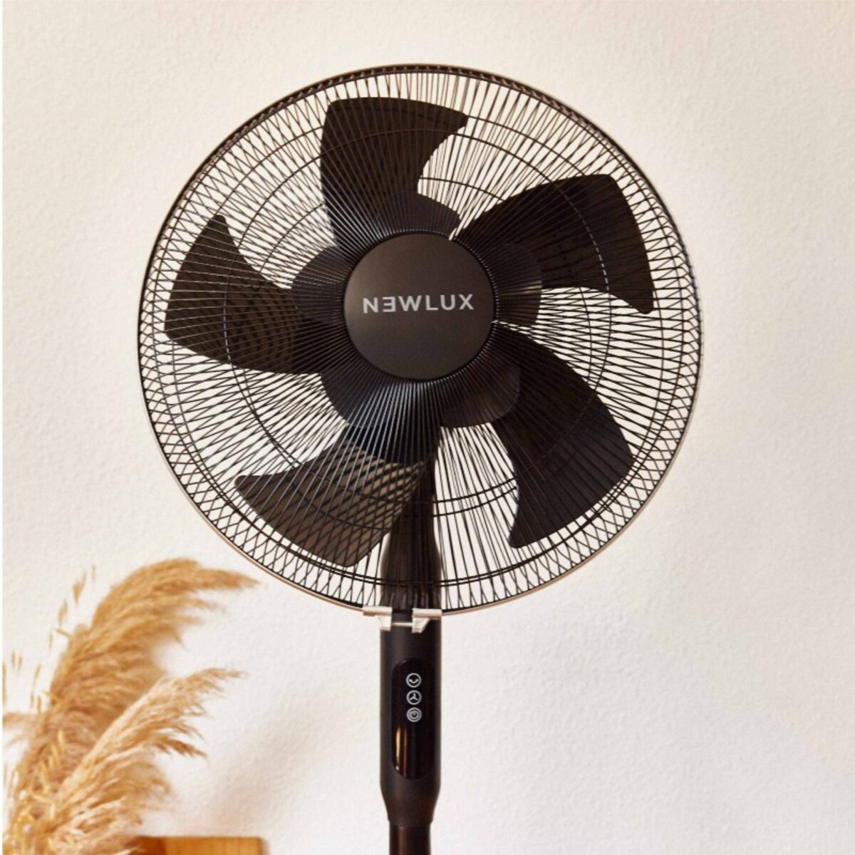Ventilador Newlux negro con jaula metálica y aspas negras, contra una pared blanca, con plantas decorativas.