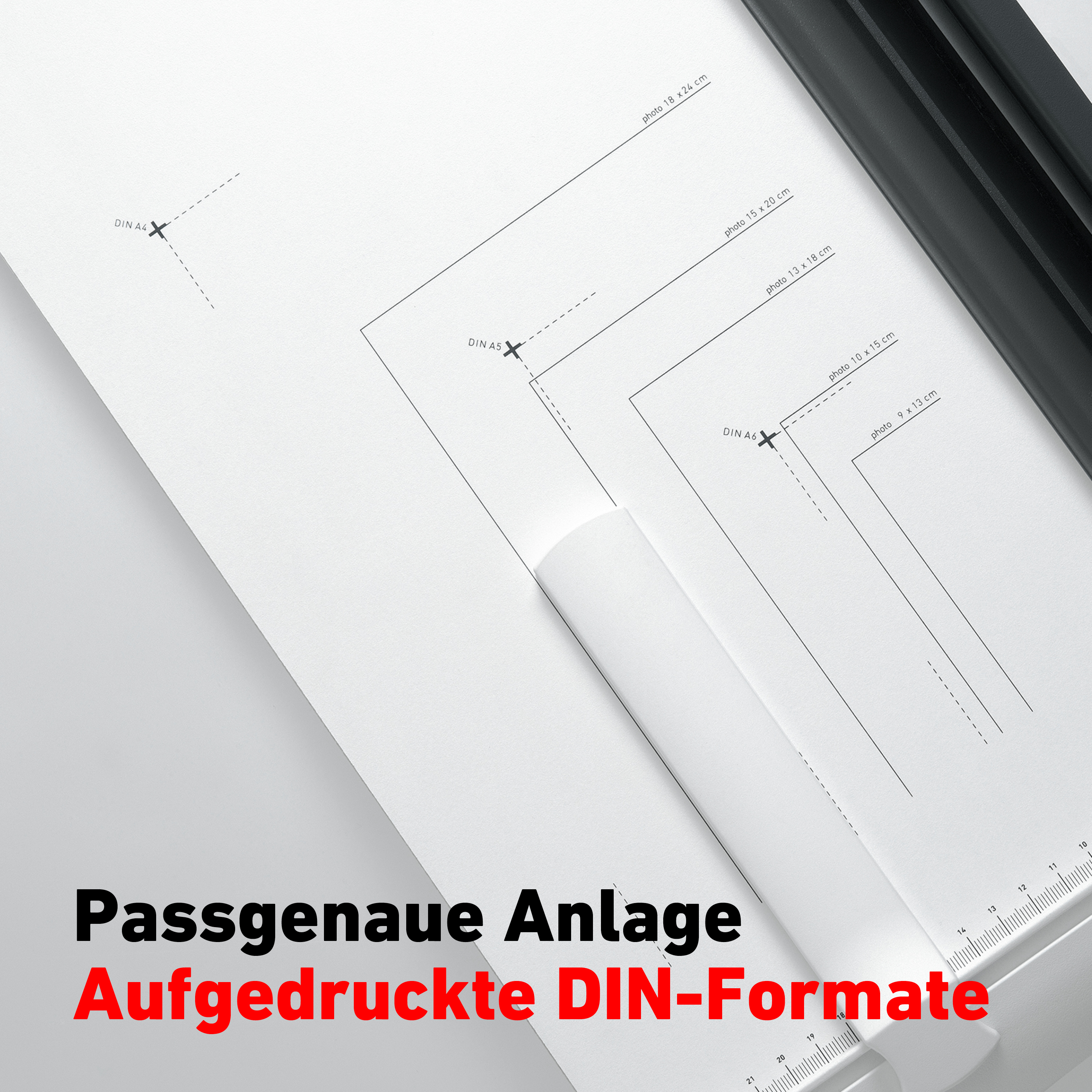 Weißes Papier mit gedruckten DIN-Formaten und einer gerollten Papierrolle. Schwarzes Schneidwerkzeug.