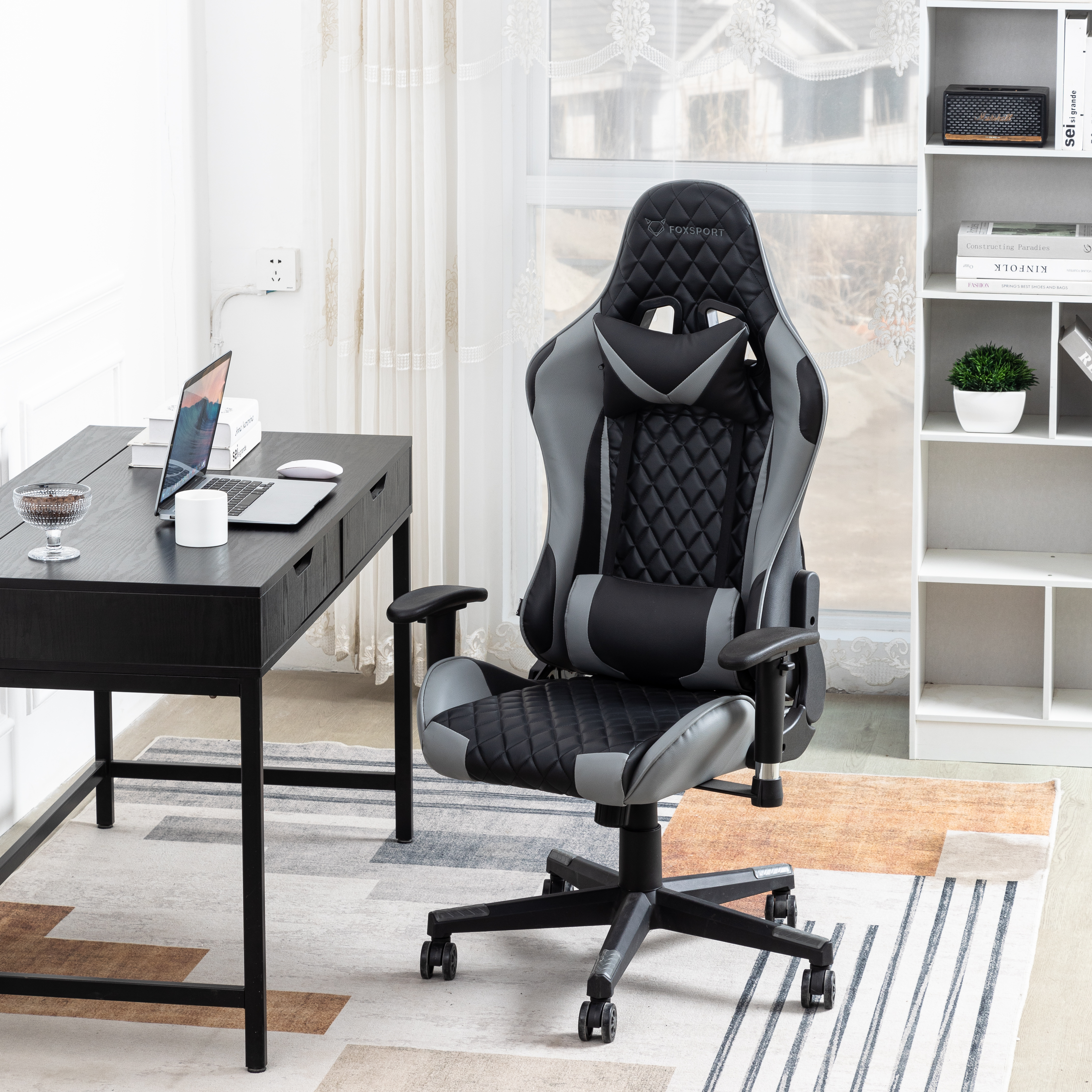 Una silla gamer en una habitación con escritorio, laptop y una estantería blanca.
