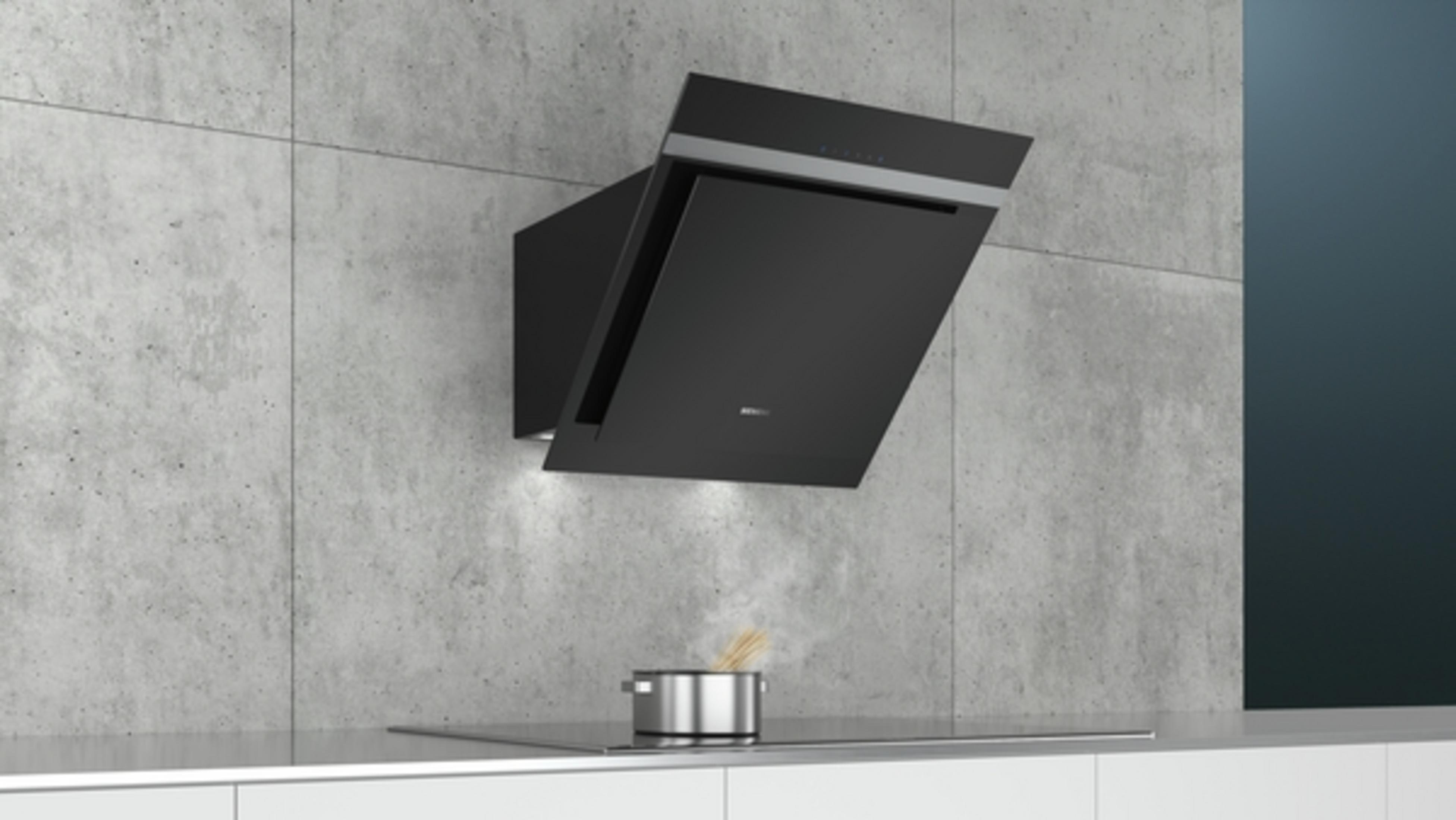 Black kitchen hood installed on a concrete wall above a stove with a pot.