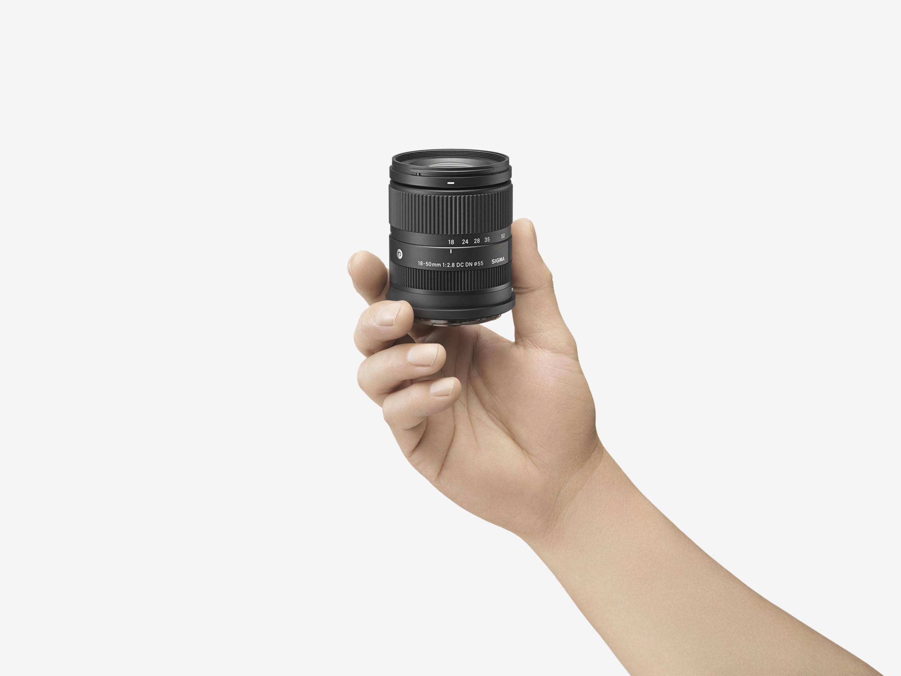 Osoba trzymająca czarny obiektyw aparatu na białym tle.
