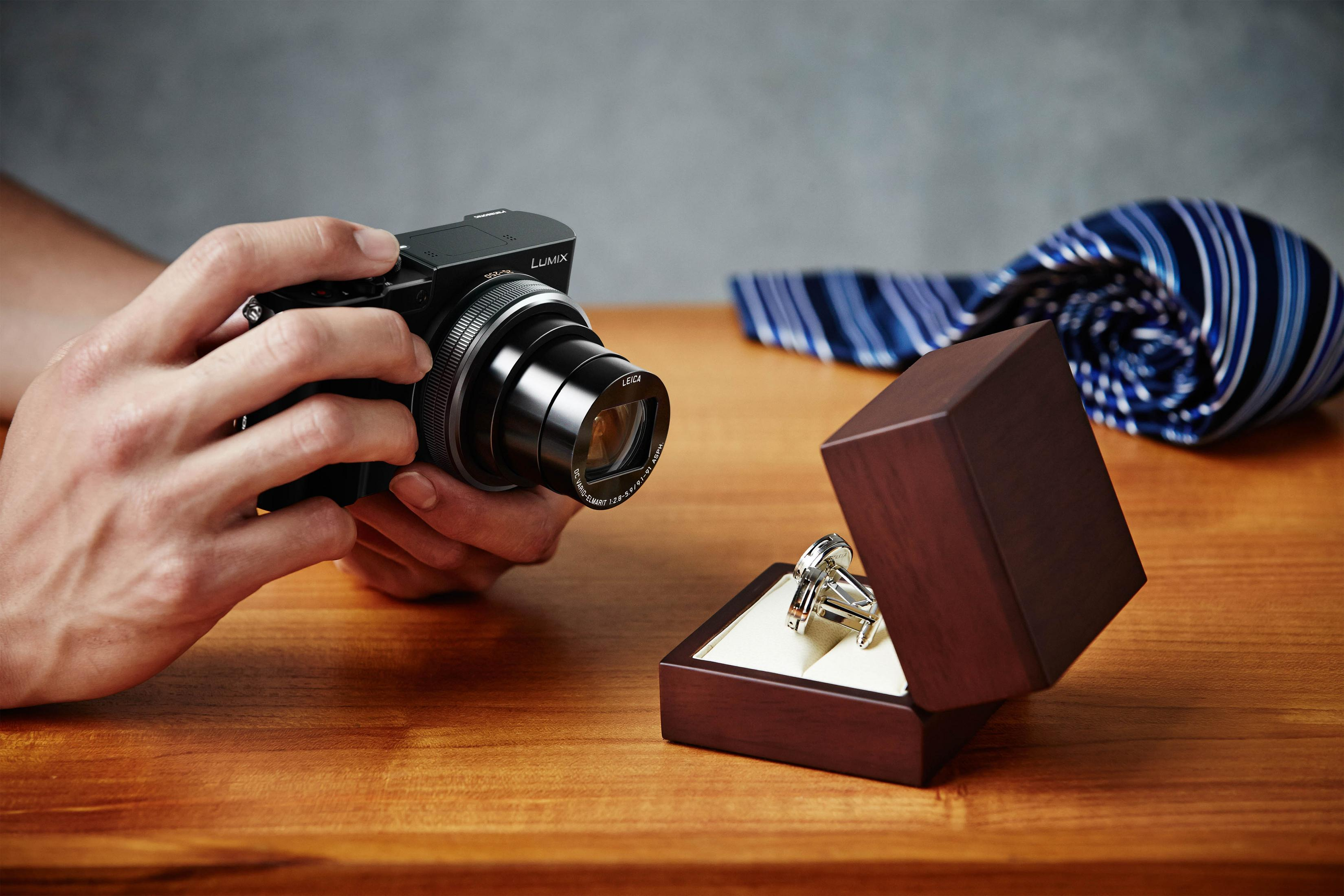 Hände halten eine Kamera, die einen Ring in einer Box fotografiert, im Hintergrund eine Krawatte.