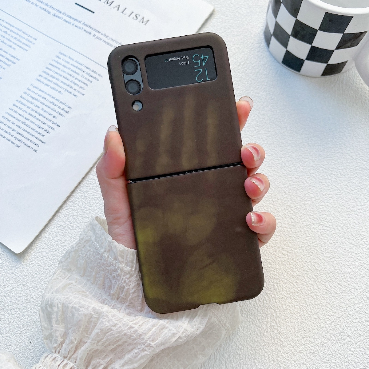 Eine braune Handyhülle auf weißer Oberfläche. Ein Telefon ist in der Hülle und zeigt Datum und Uhrzeit.