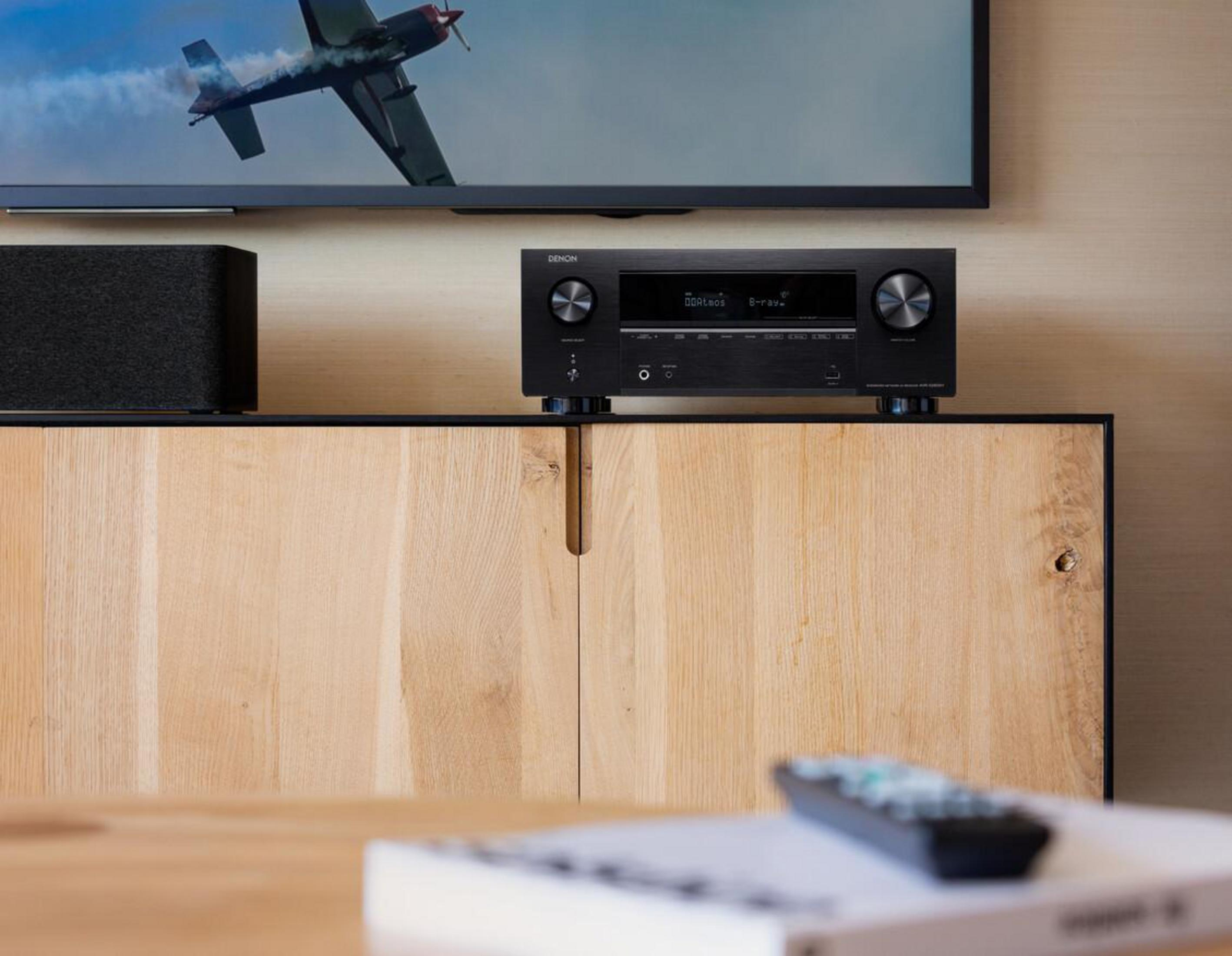 Sala de estar con televisor, sistema de sonido y armario. Un mando a distancia está colocado sobre un libro.
