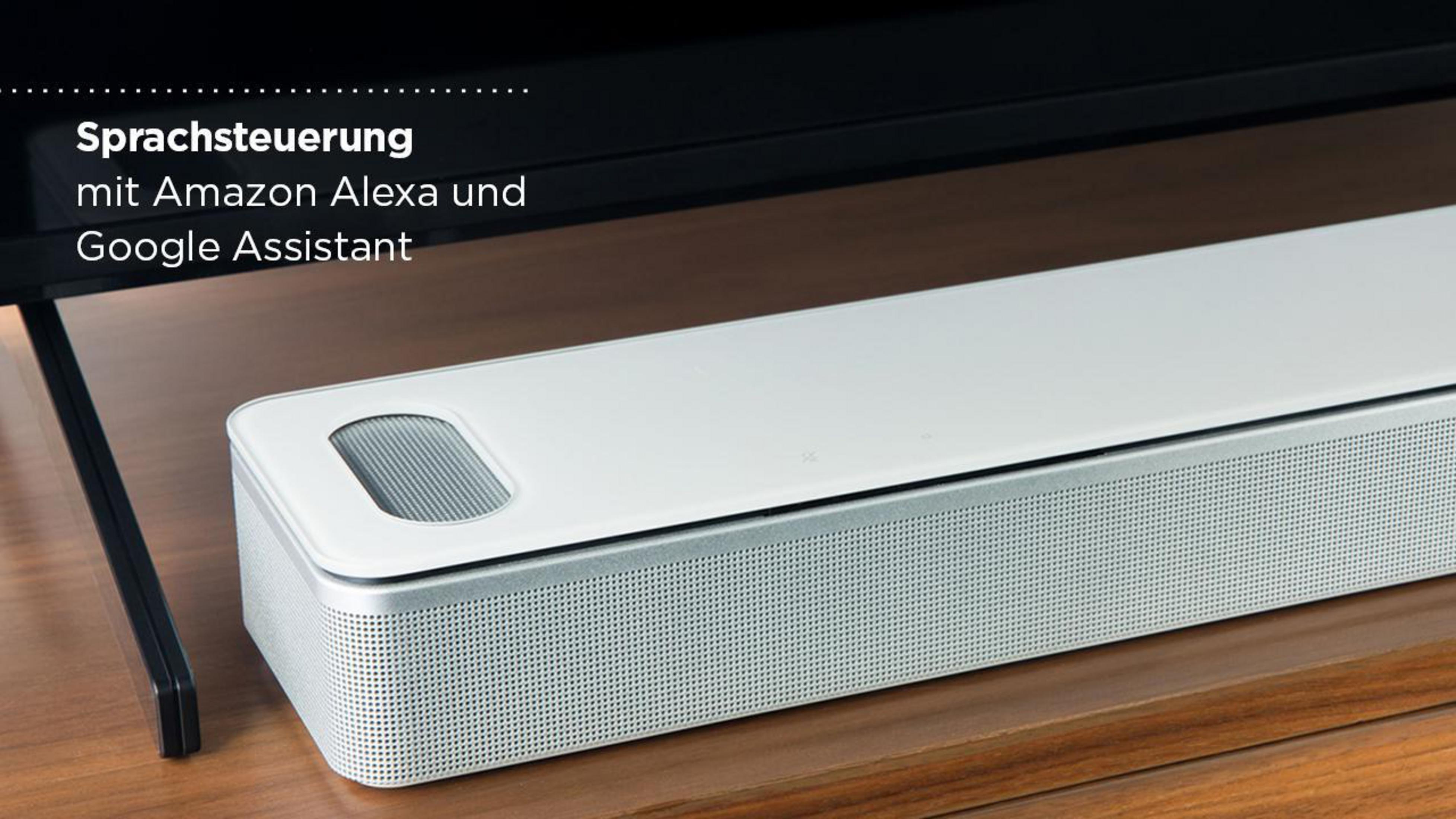 Weiße Soundbar auf Holzoberfläche. Text-Overlay: Sprachsteuerung mit Amazon Alexa und Google Assistant.