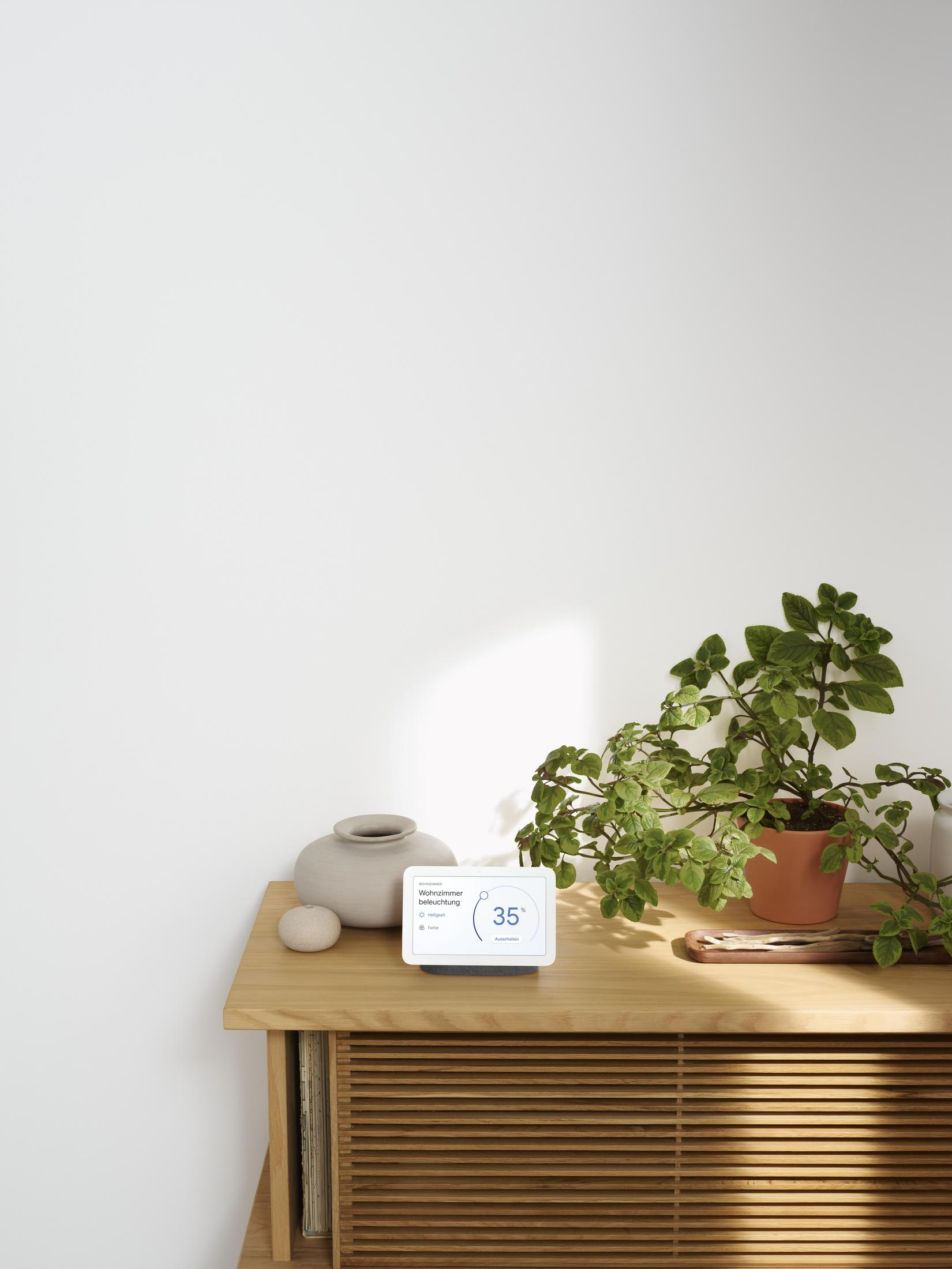 Un dispositivo intelligente su legno, con pianta e vaso. Il muro è bianco.