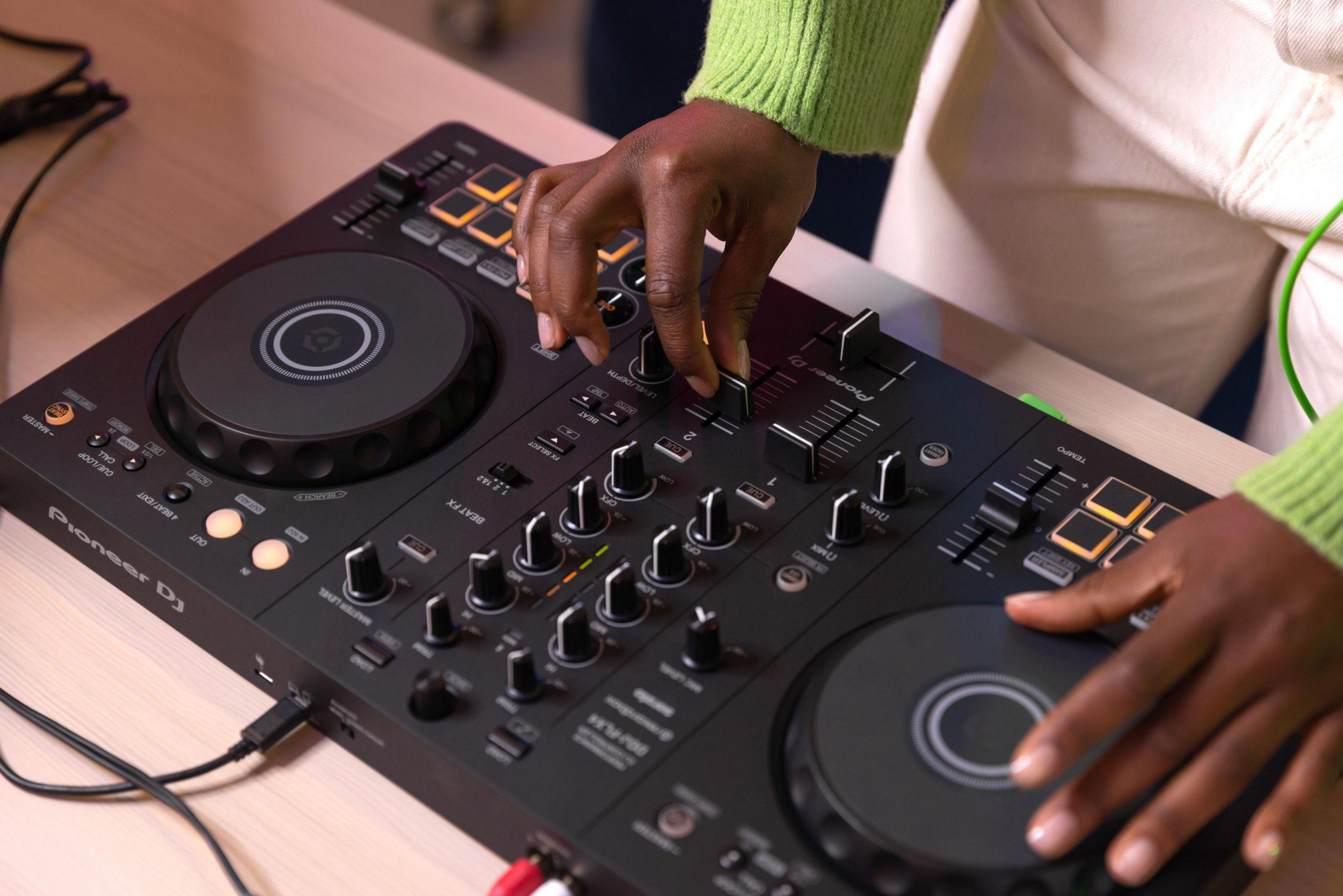 Hände einer Person auf einem schwarzen Pioneer DJ-Controller mit verschiedenen Knöpfen und Tasten, in einem hellen Raum.