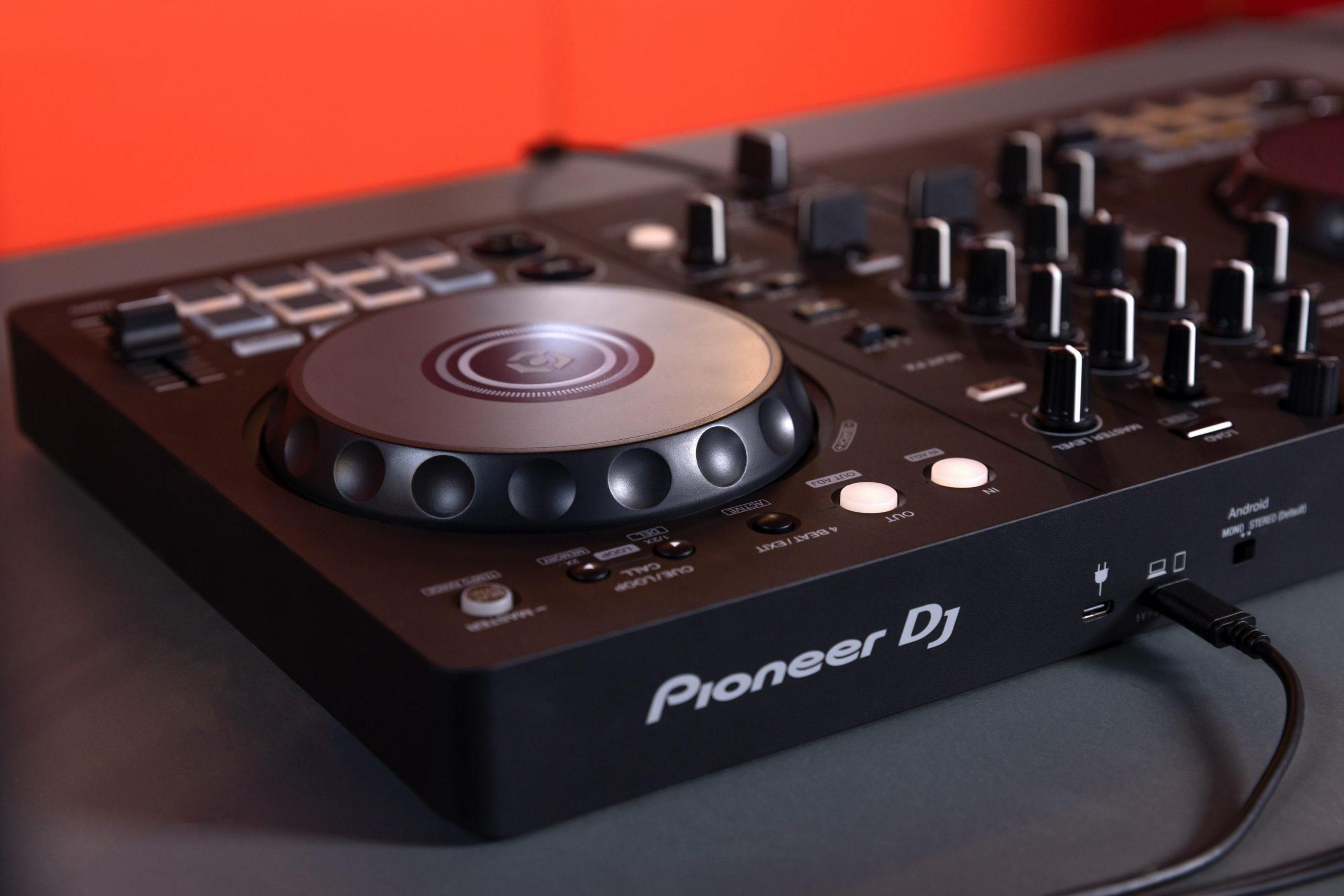 Nahaufnahme eines DJ-Controllers mit Knöpfen, Jogwheel und dem Pioneer DJ-Logo. Schwarze Oberfläche und oranger Hintergrund.