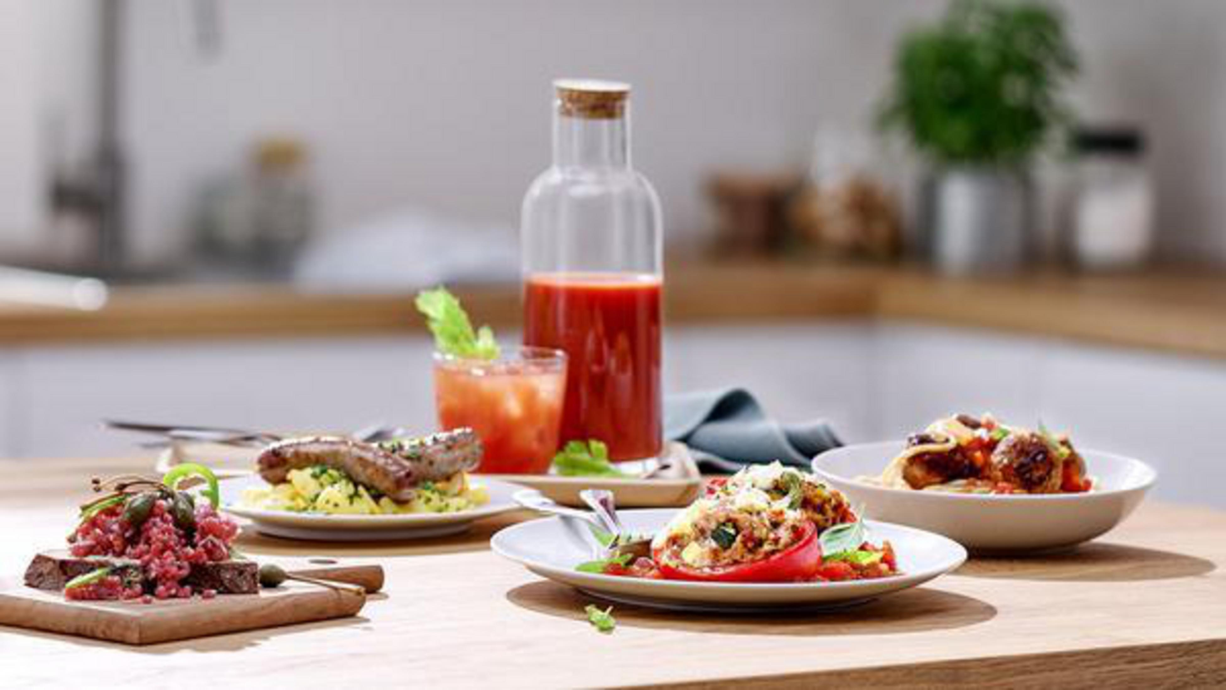 Różne dania z jedzeniem na drewnianym stole. Butelka soku pomidorowego pośrodku.