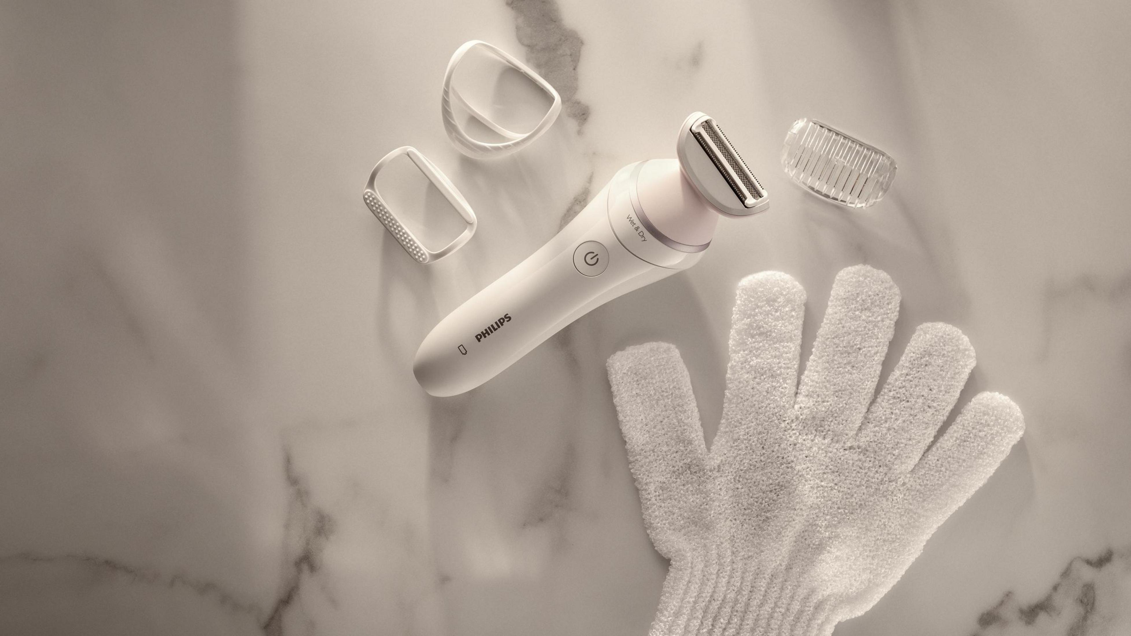 Afeitadora eléctrica Philips blanca con accesorios y un guante blanco sobre mármol.