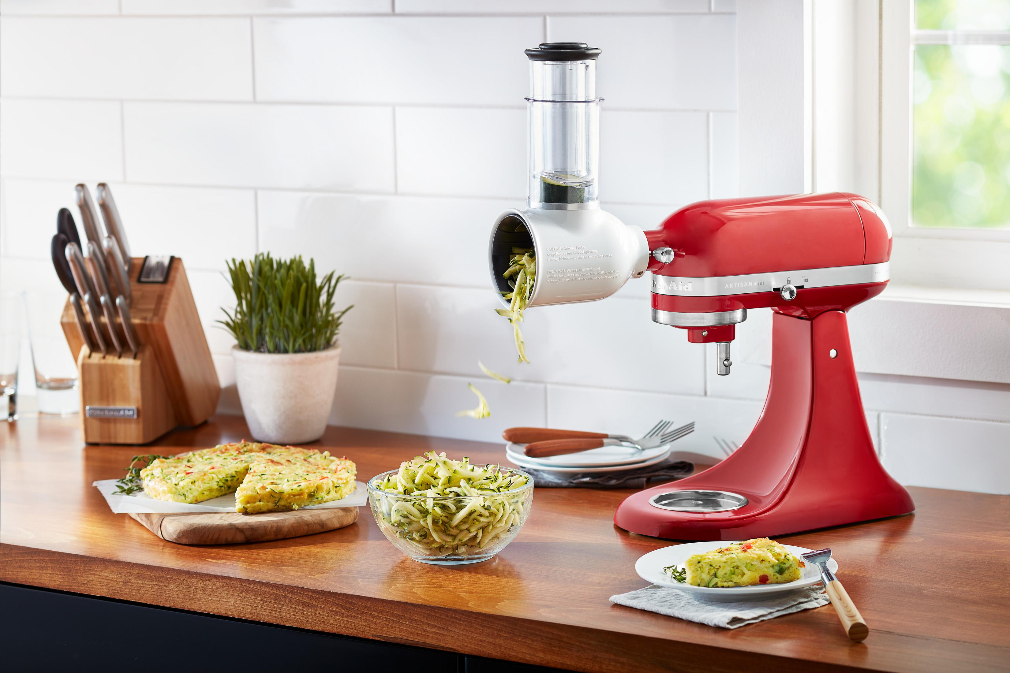 Roter KitchenAid-Mixer zerkleinert Gemüse neben Sandwiches.