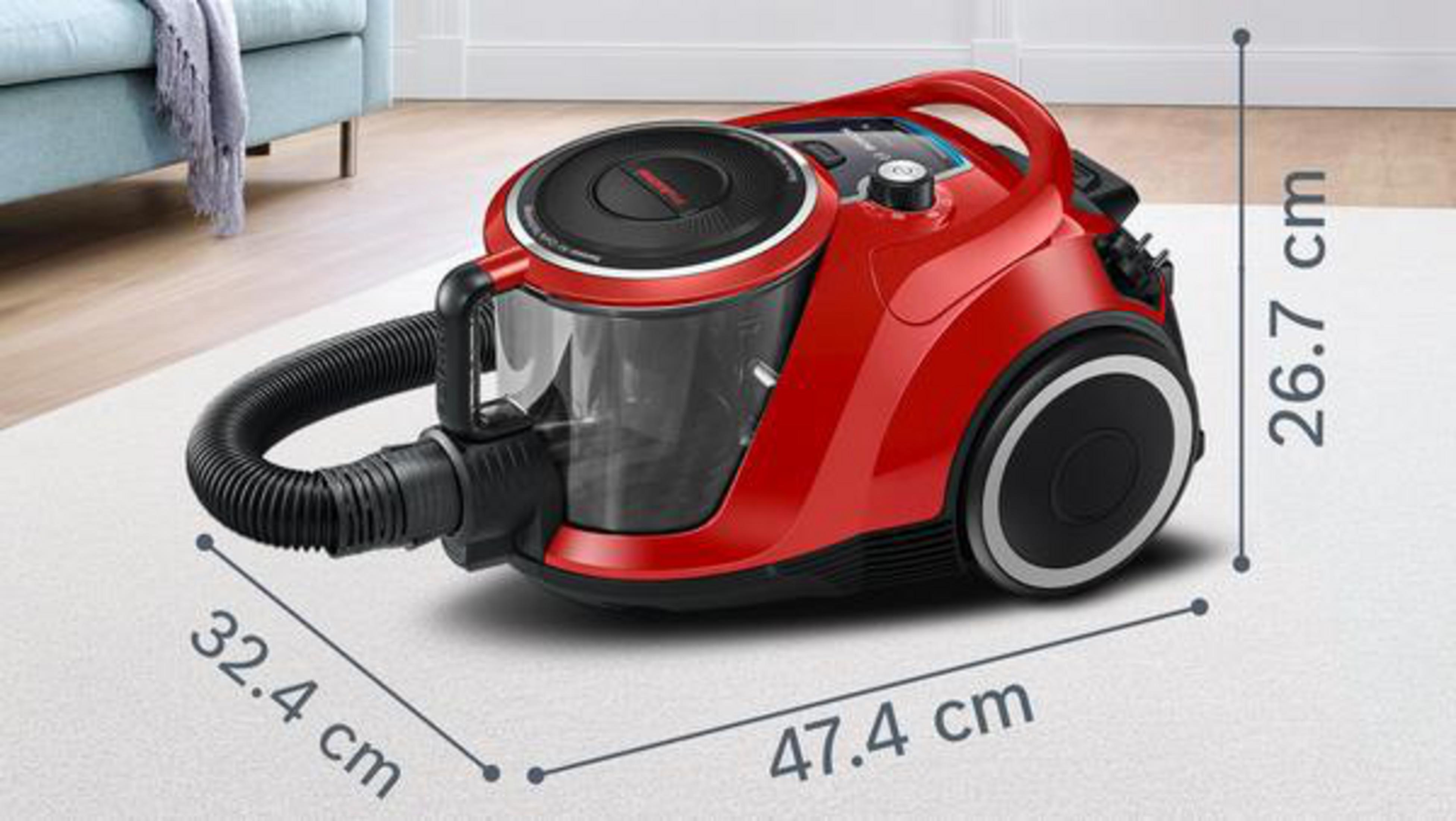 Czerwony odkurzacz z wymiarami na białym dywanie i sofa w tle.