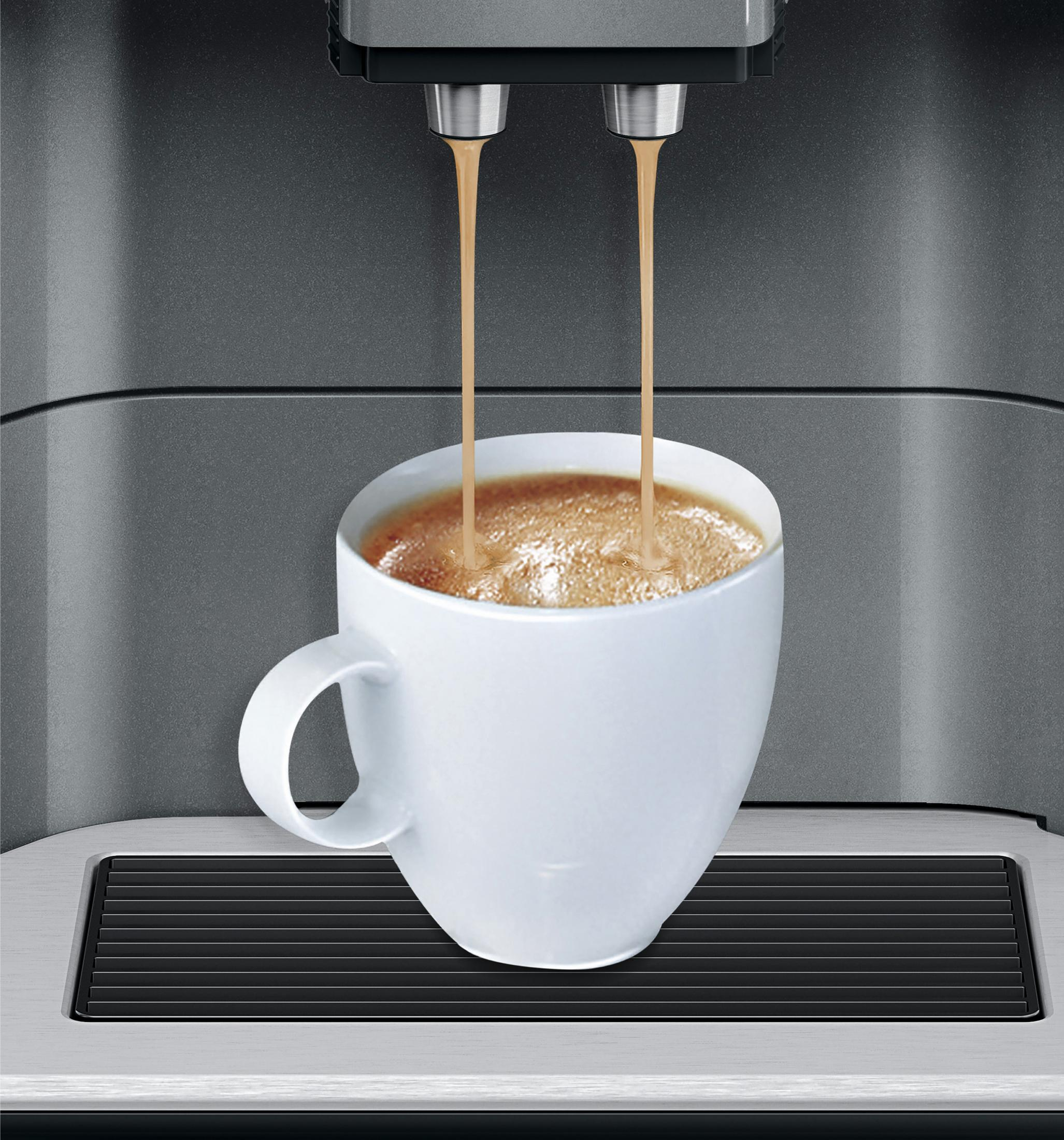 Una tazza bianca viene riempita di caffè da una macchina da caffè. La macchina da caffè è grigia.