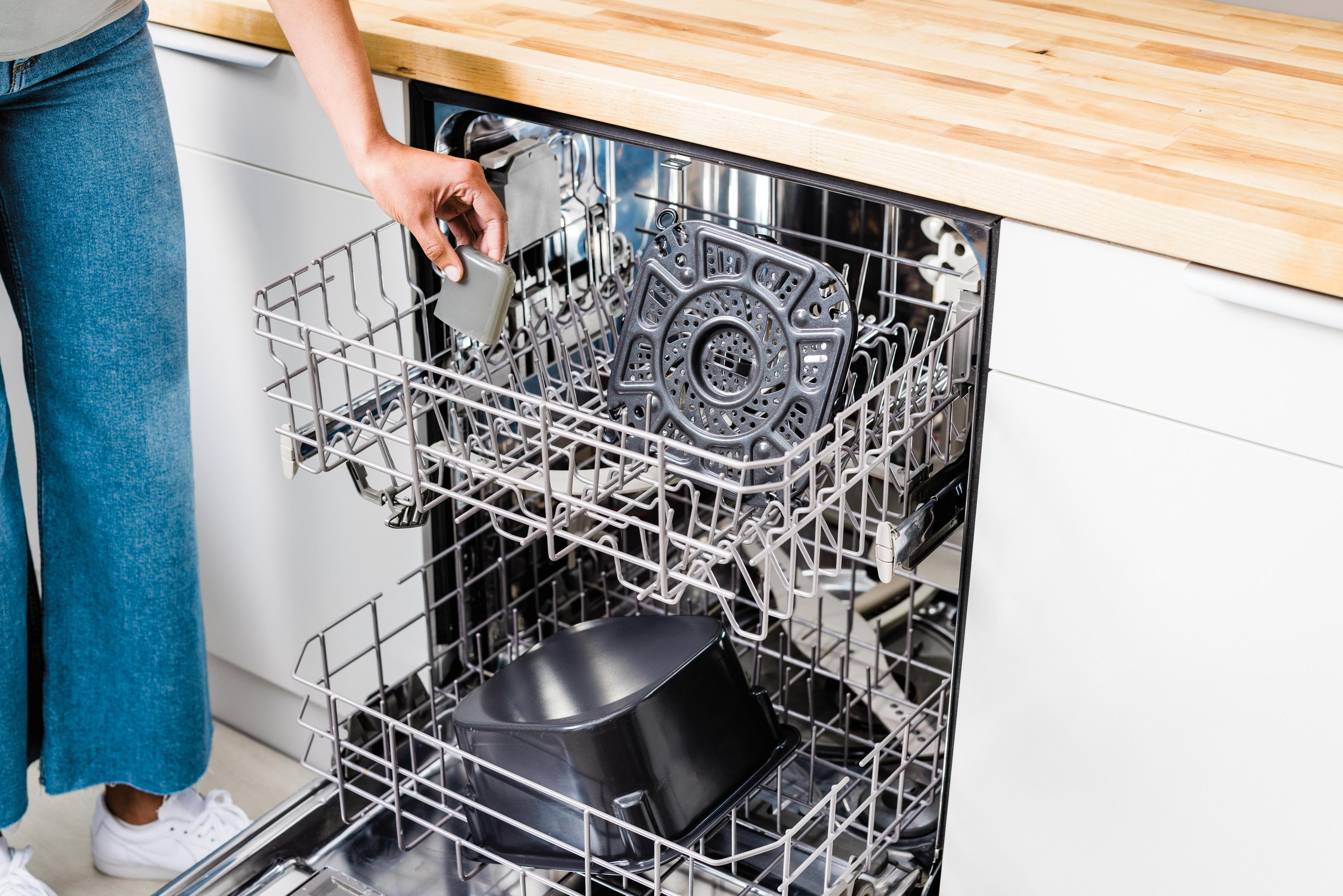 Osoba umieszcza przedmiot w zmywarce. Zmywarka jest otwarta z przedmiotami w środku.