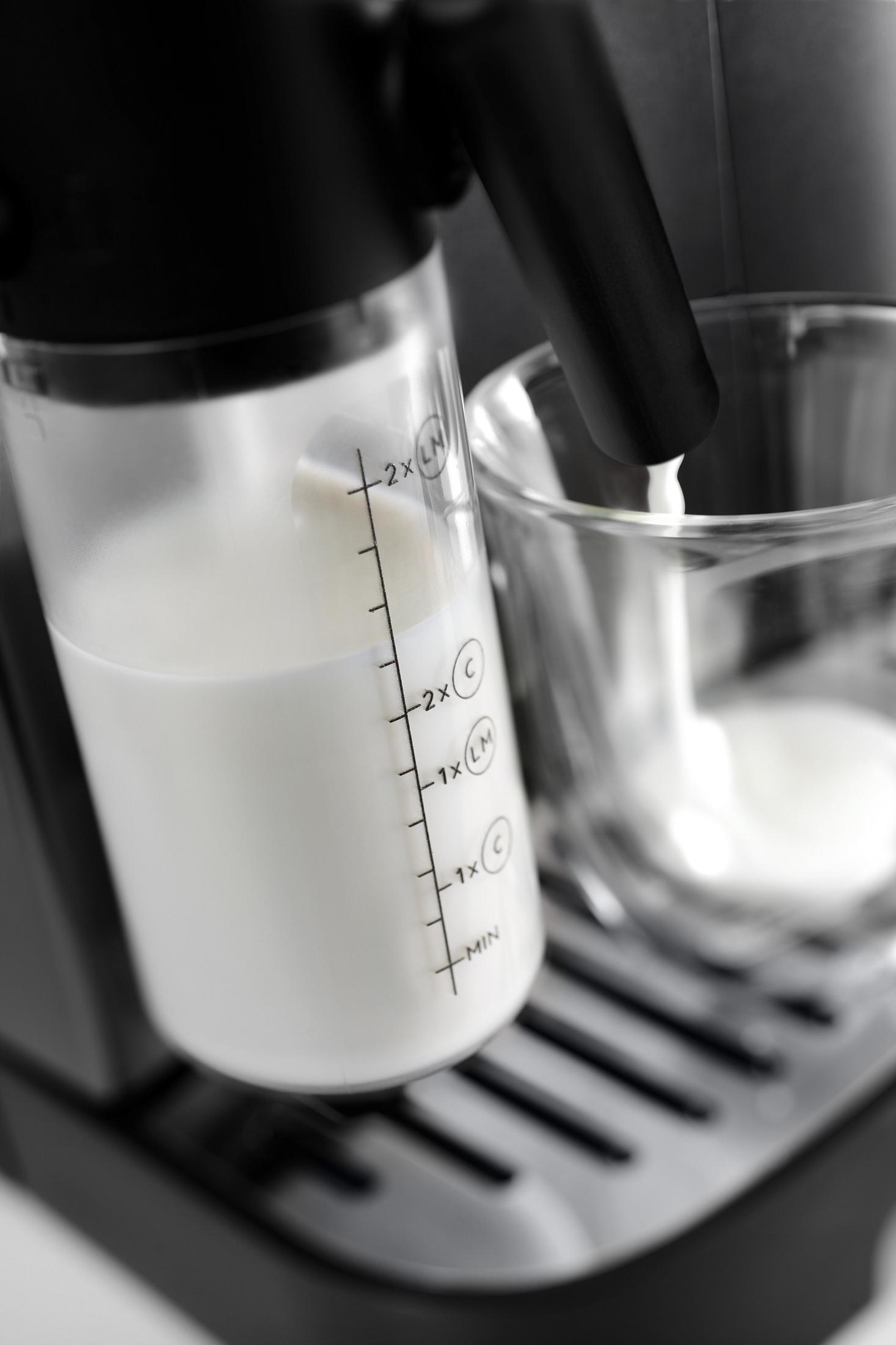 Mleko wlewa się z przezroczystego pojemnika do szklanki, część ekspresu do kawy, zbliżenie.