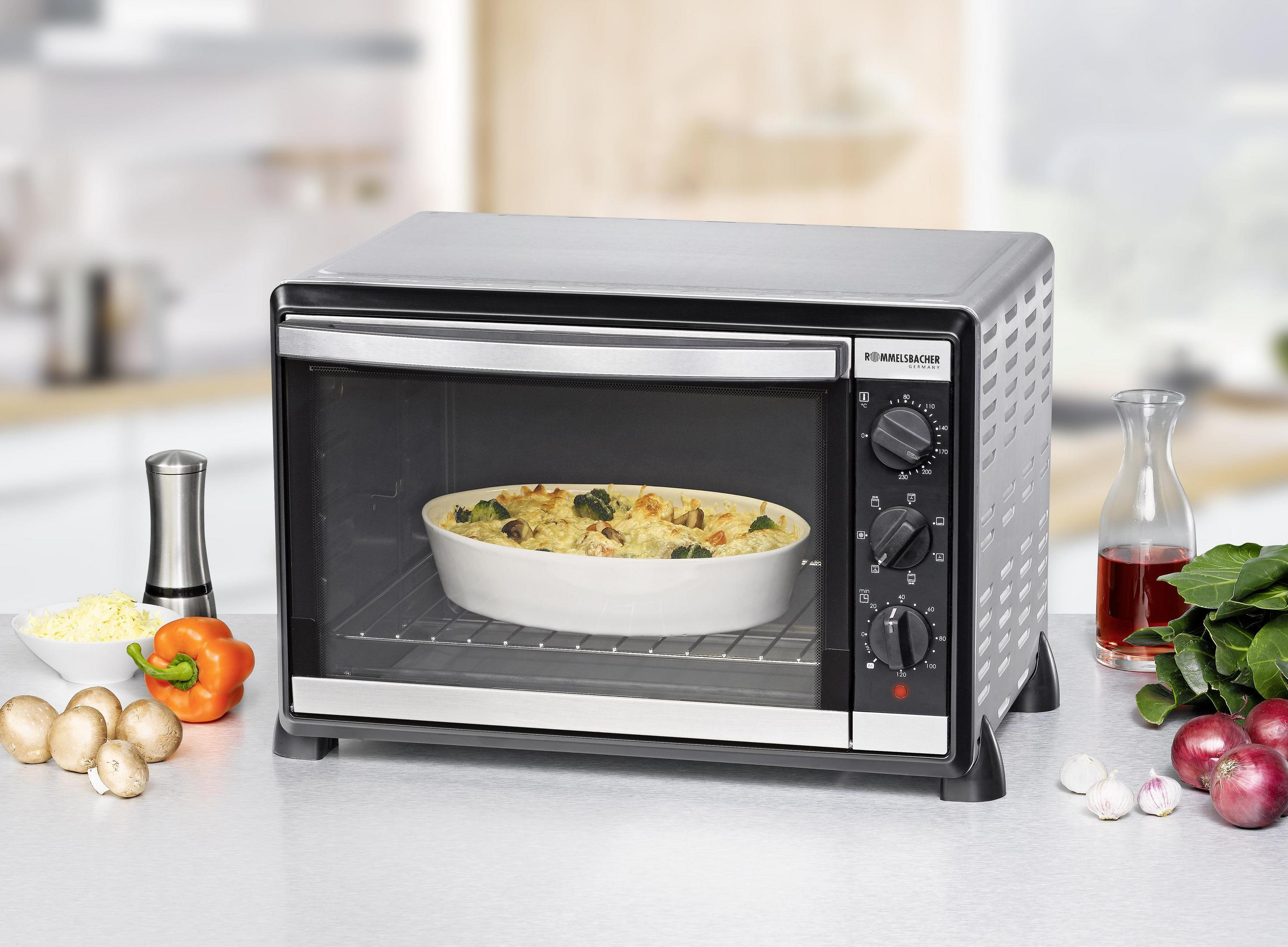 Srebrny piekarnik z jedzeniem w środku. Pomarańczowa papryka, pieczarki i pomidory na blacie. Jasna kuchnia.