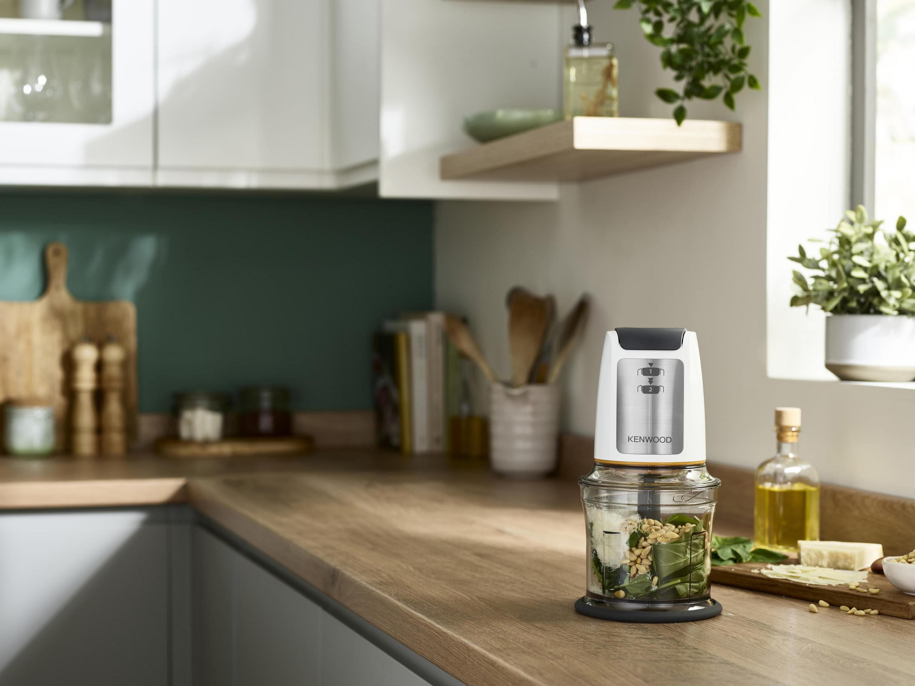 Eine Küchenszene mit einem Food Processor auf einer hölzernen Arbeitsplatte, in der Nähe eines Fensters.