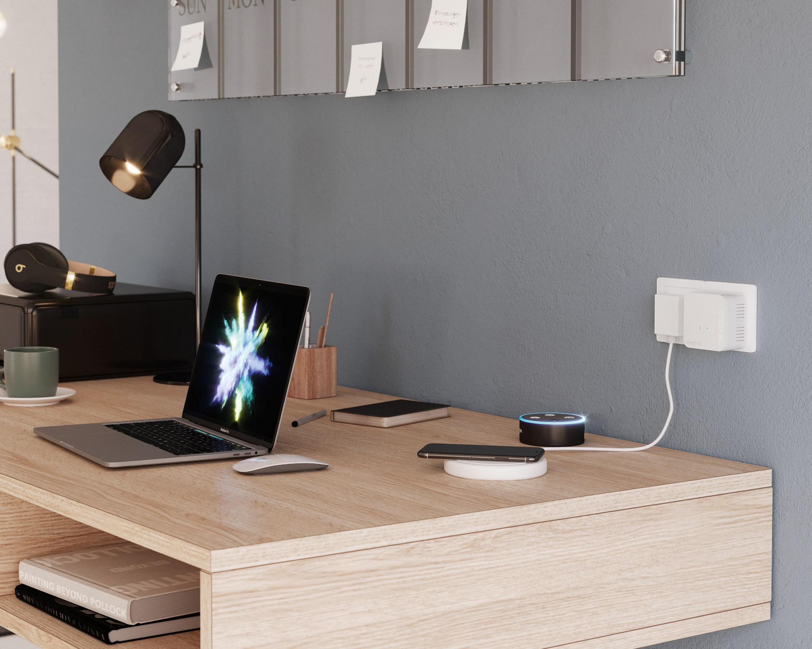 Konfiguracja biurka z laptopem, telefonem, ładowarką bezprzewodową, inteligentnym głośnikiem i słuchawkami. Szara ściana.